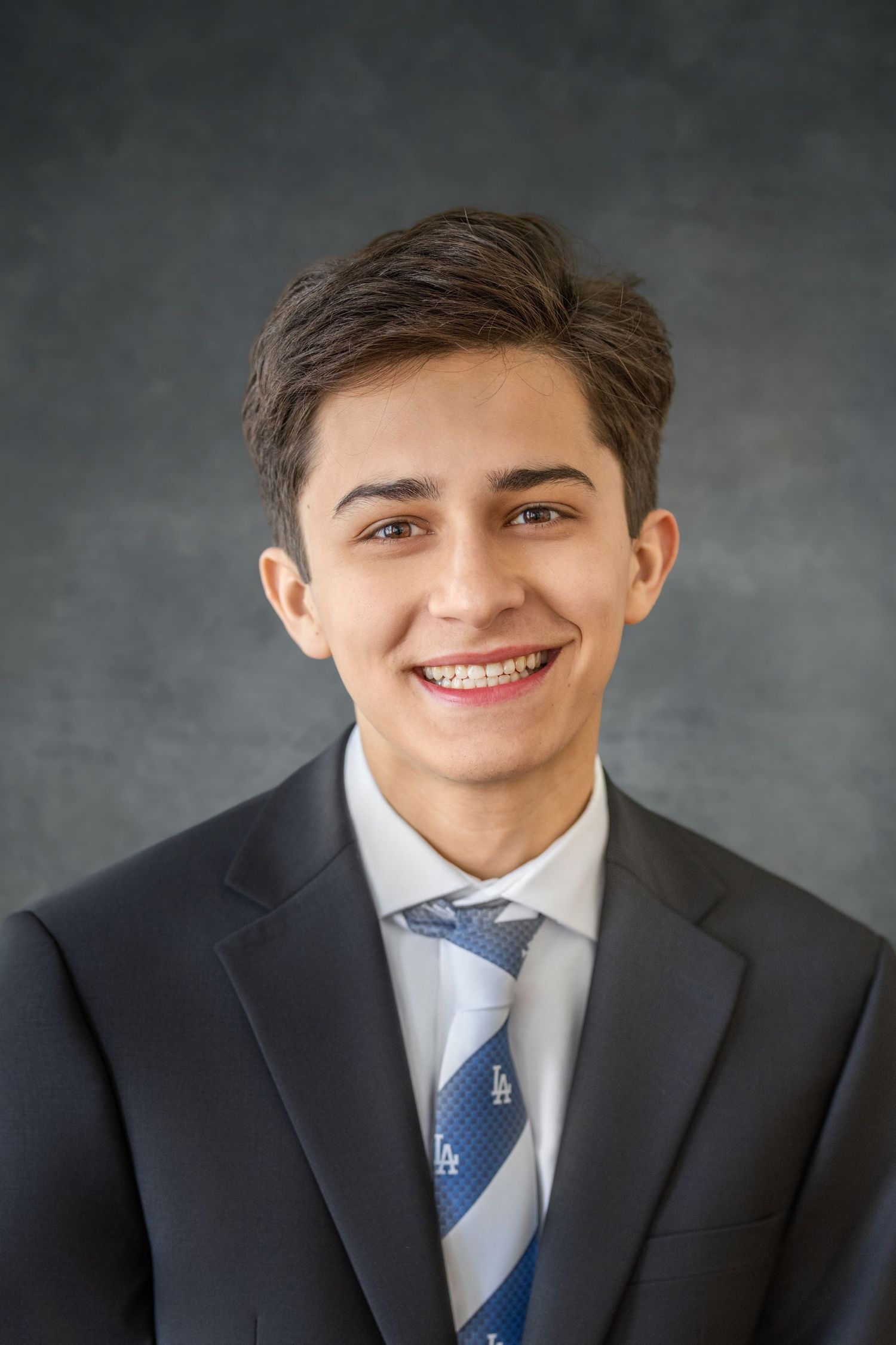Professional headshot portrait in a dark suit and blue patterned tie against a gray backdrop. Yearbook photos for senior.