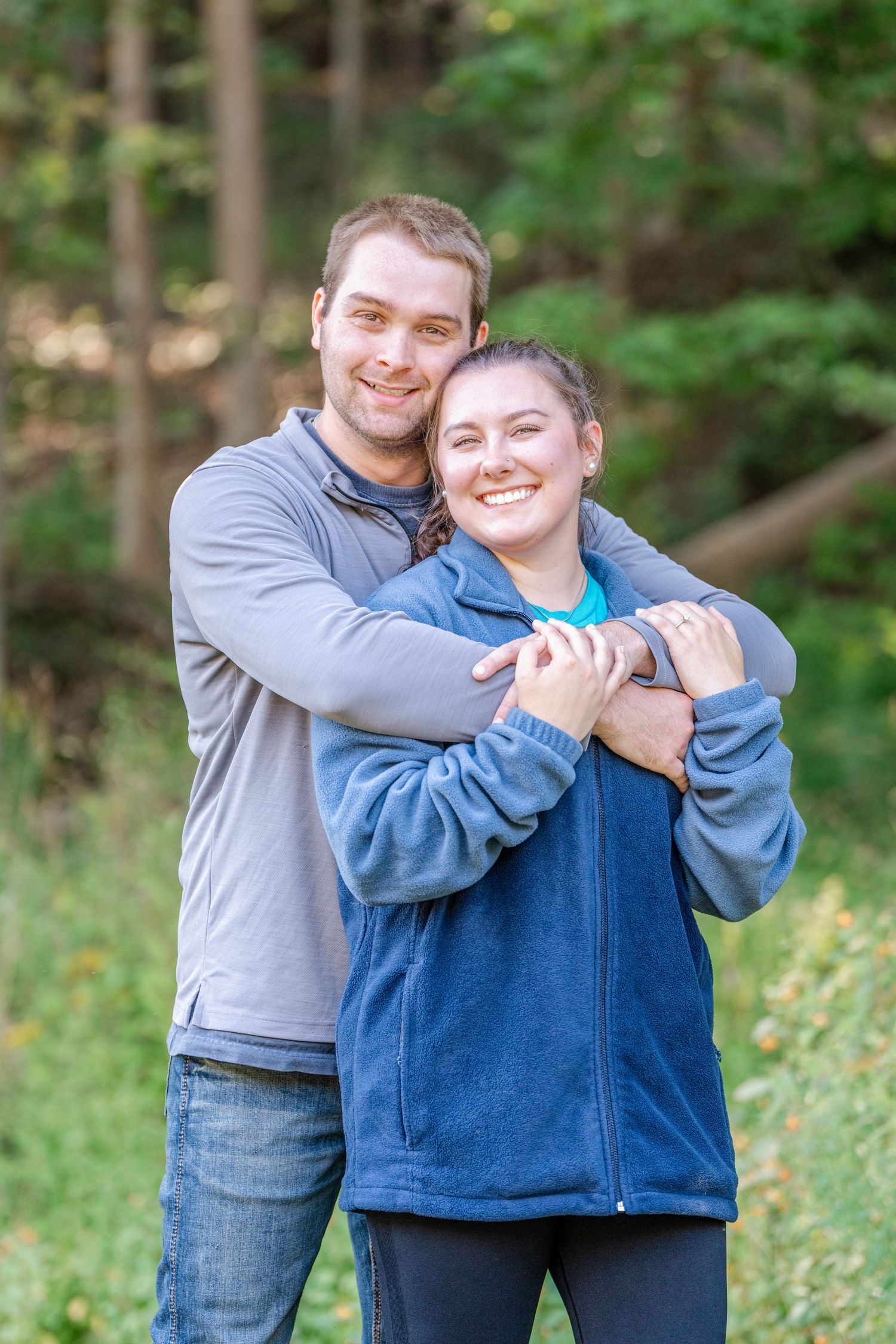 A couple embraces and laughs together in a lush green forest setting.