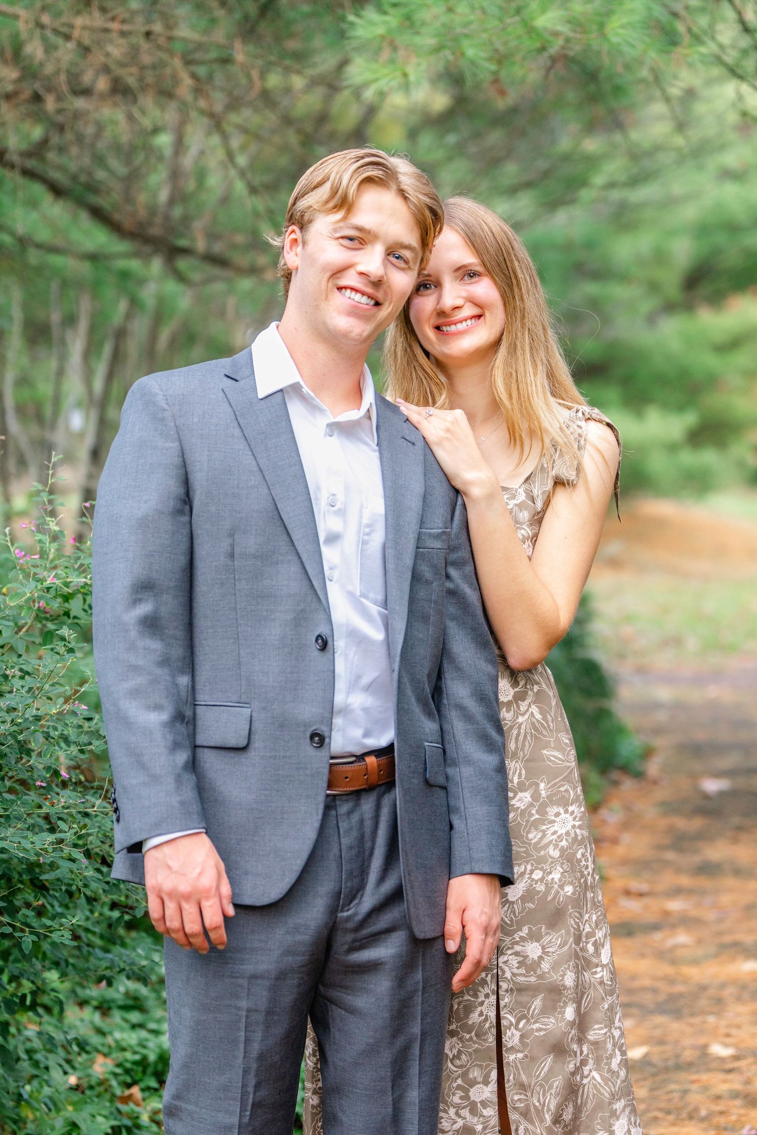 A couple shares a joyful moment together on a wooded path while wearing formal attire.