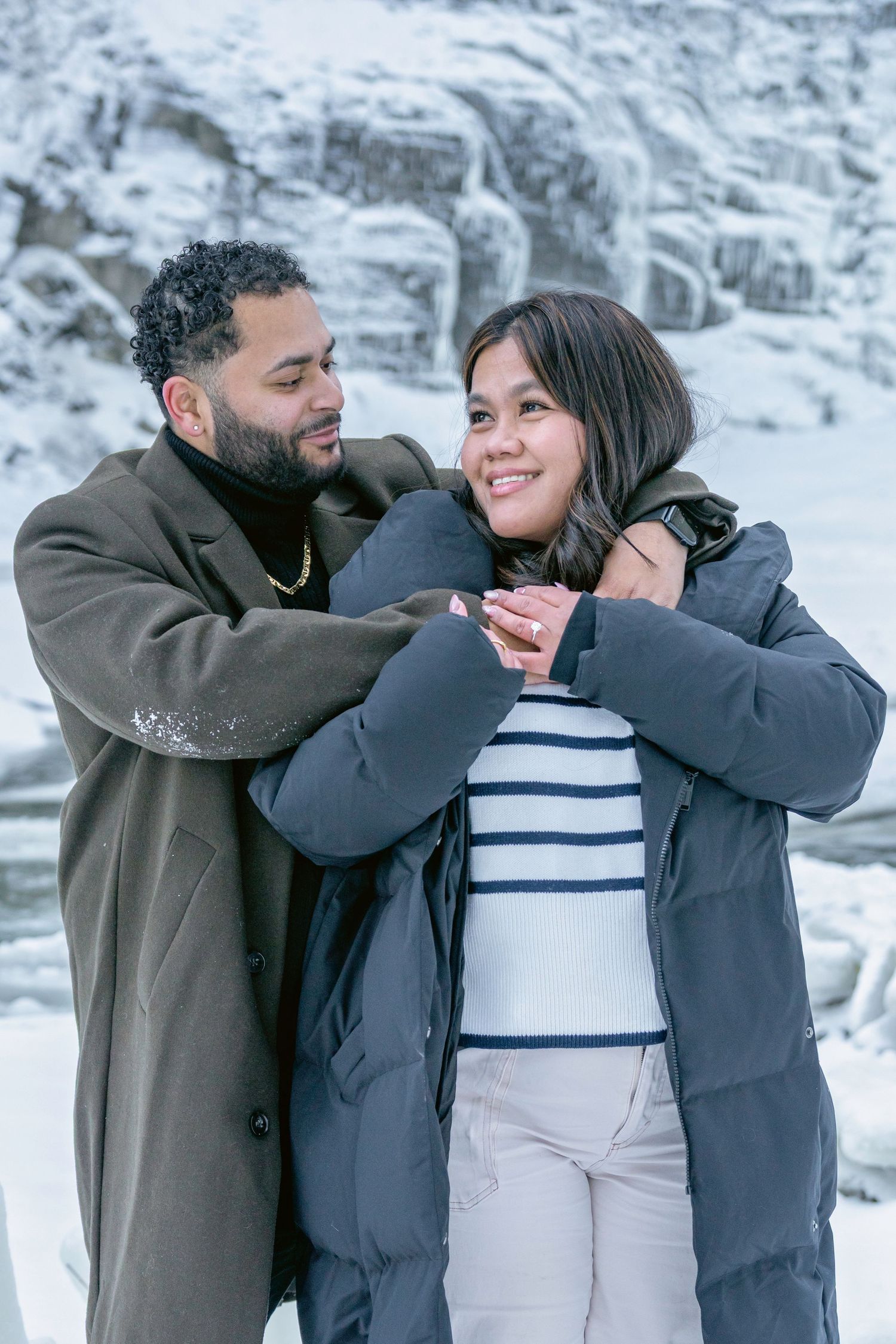A couple shares a playful moment together while wearing winter coats in a snowy outdoor setting.