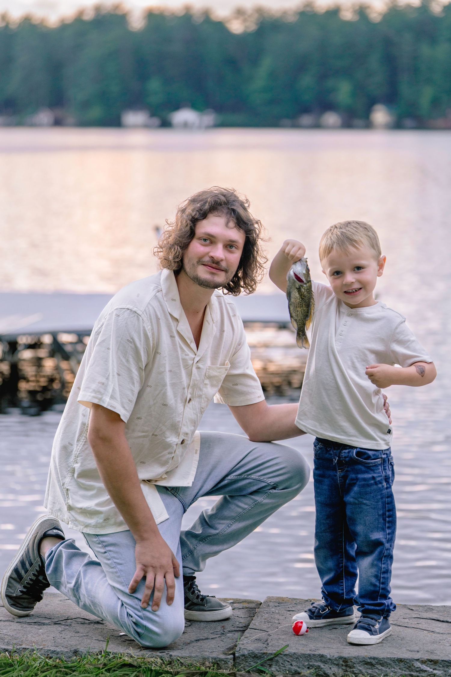 A proud fishing moment captured on a lakeside dock as they display their freshly caught fish at sunset.