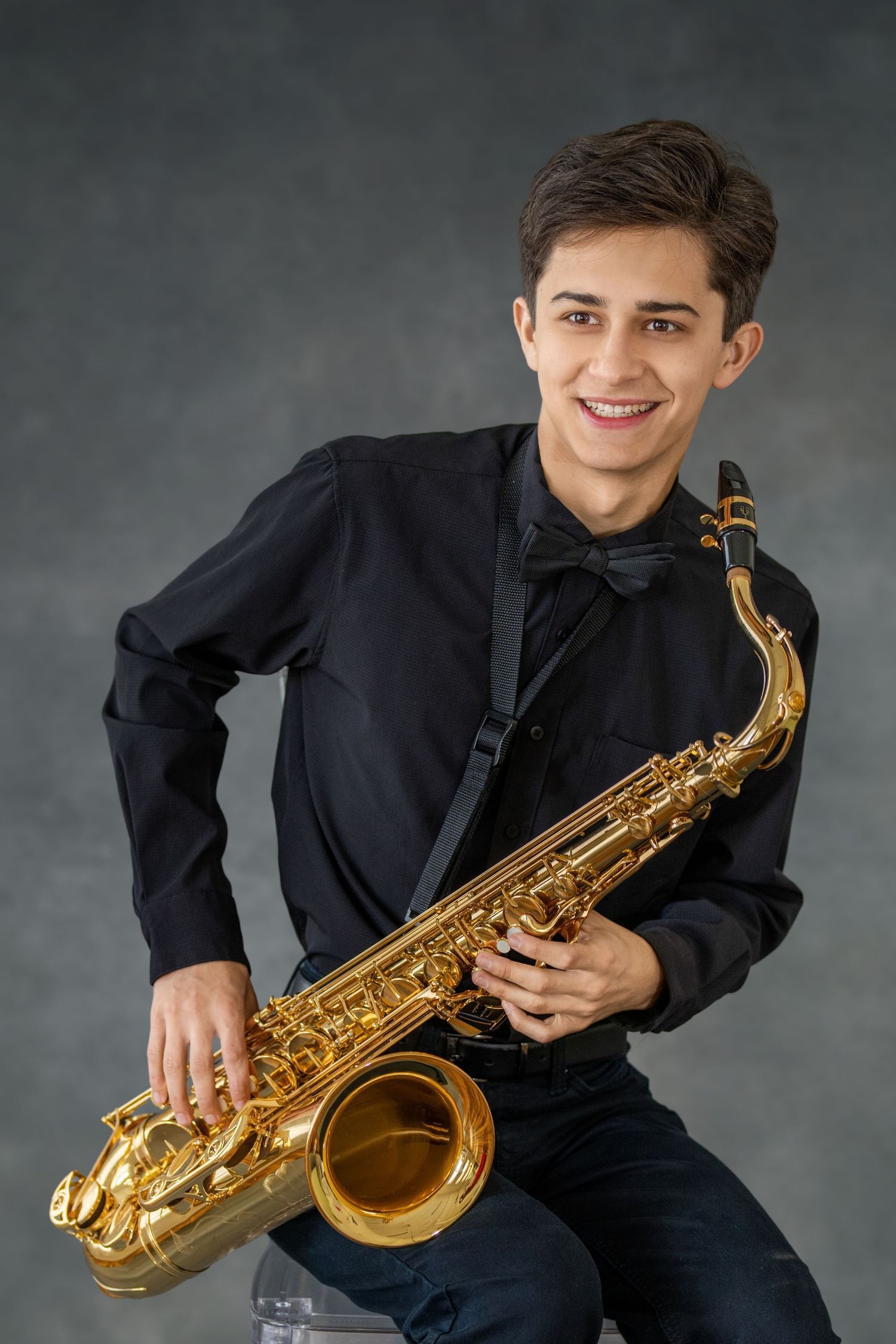 Musician in black attire plays alto saxophone against grey backdrop in artistic portrait series.