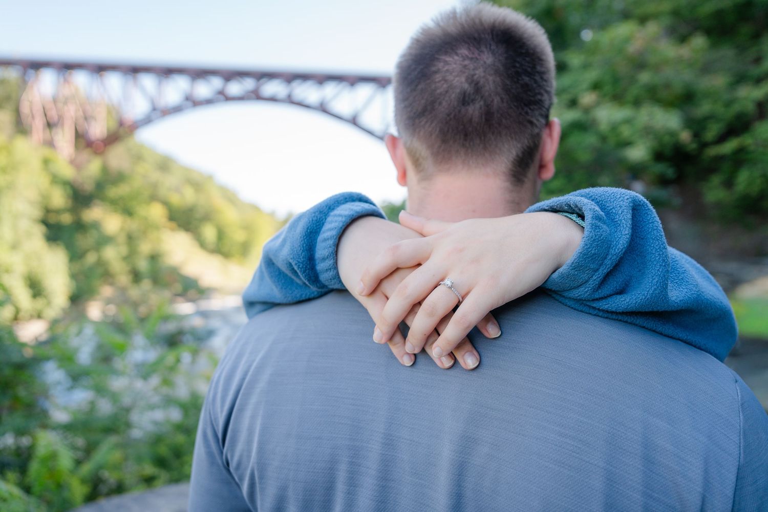 A couple shares an intimate moment together while standing on a path surrounded by greenery and nature.
