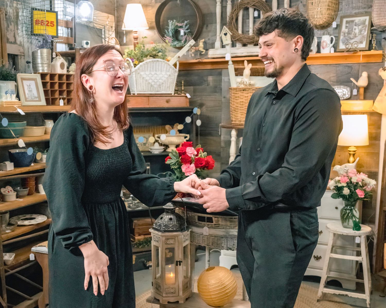 Man presenting flowers to laughing woman in a charming antique shop filled with rustic decor.