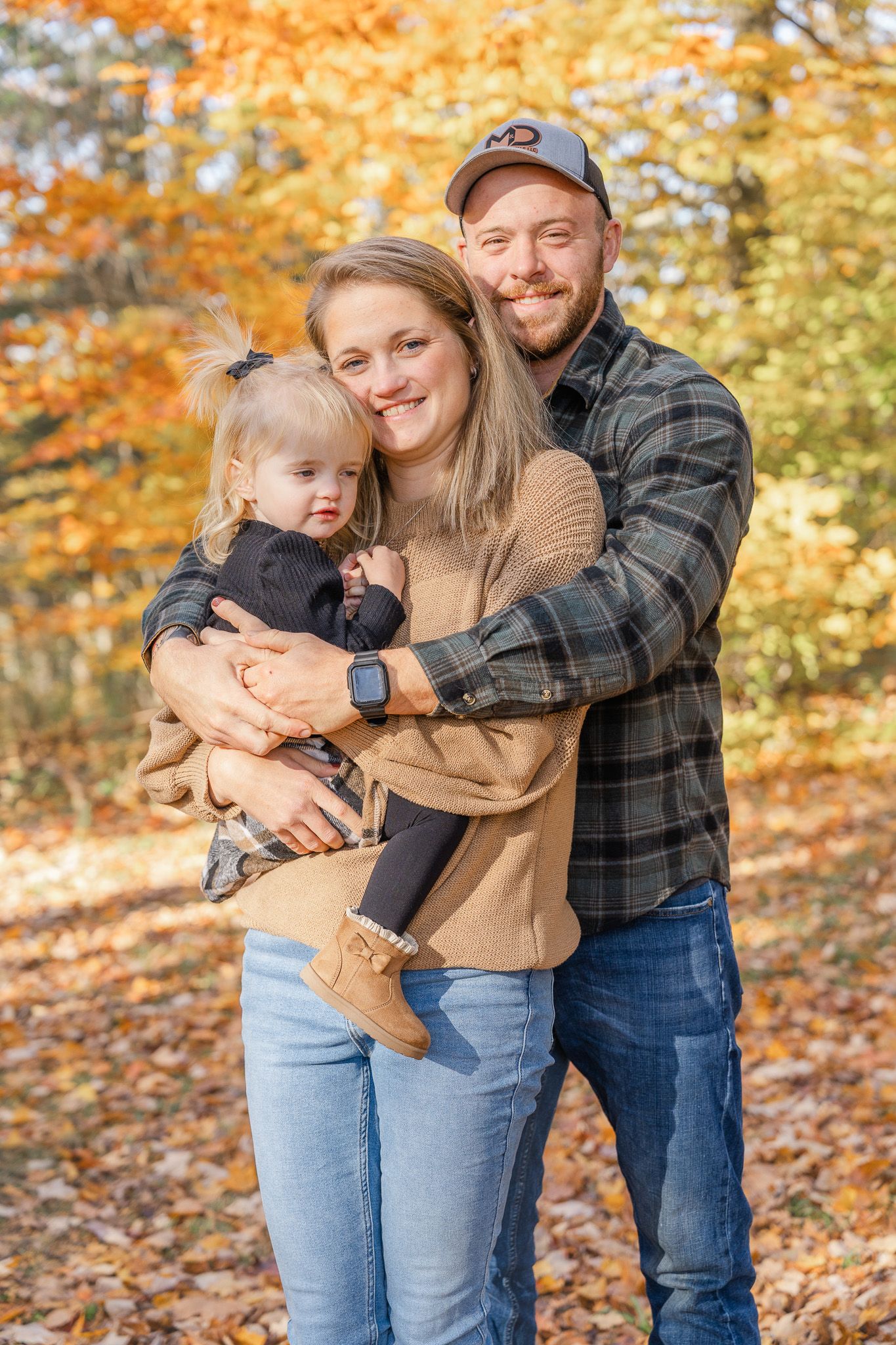 Family embraces and plays with their baby against a backdrop of vibrant fall leaves in the woods.