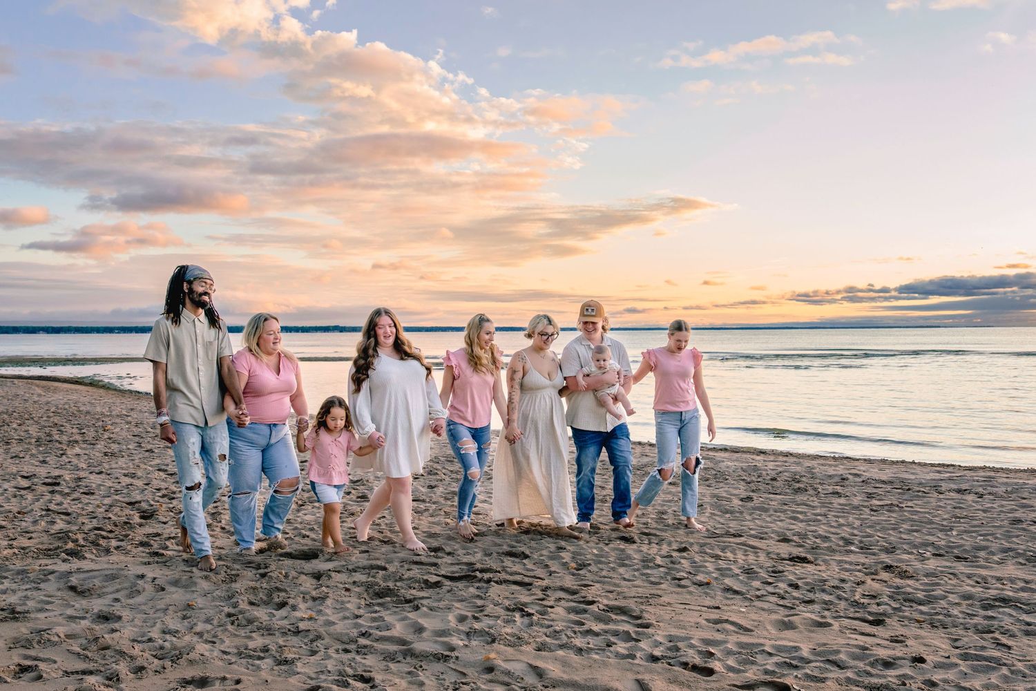 Family group walking together on sandy beach at sunset with colorful sky and ocean waves in background.