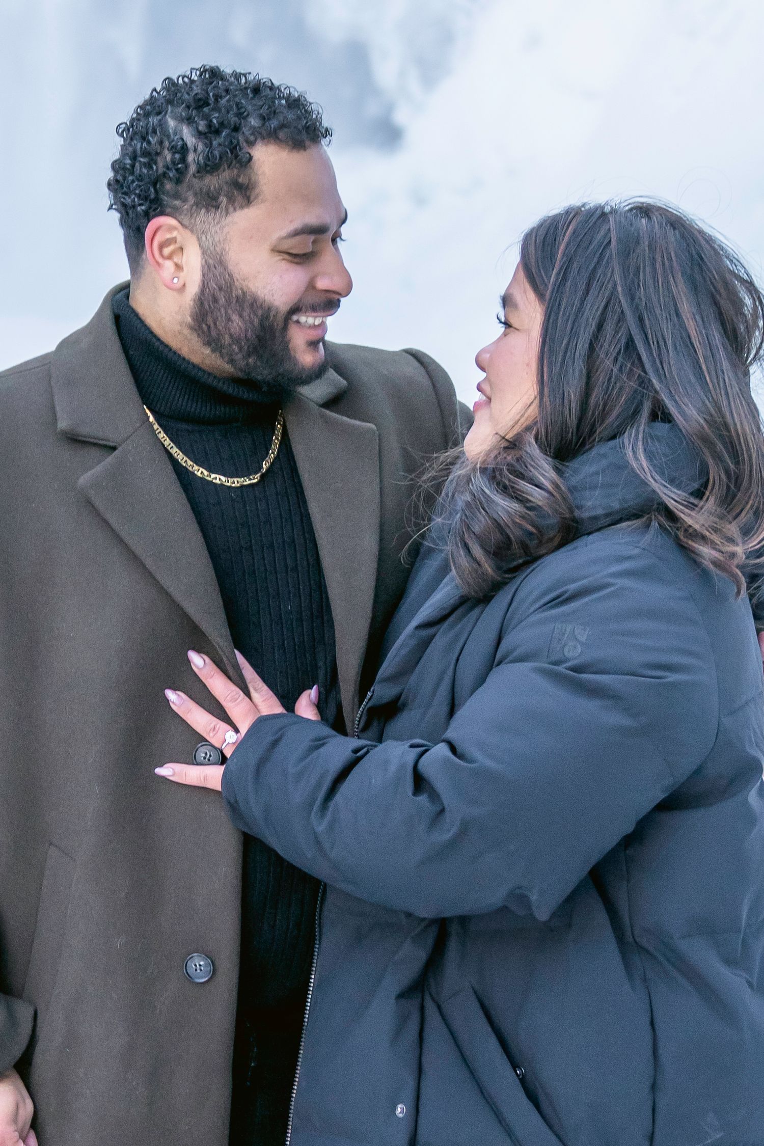 A couple in winter coats share a joyful moment together while laughing and embracing outdoors.
