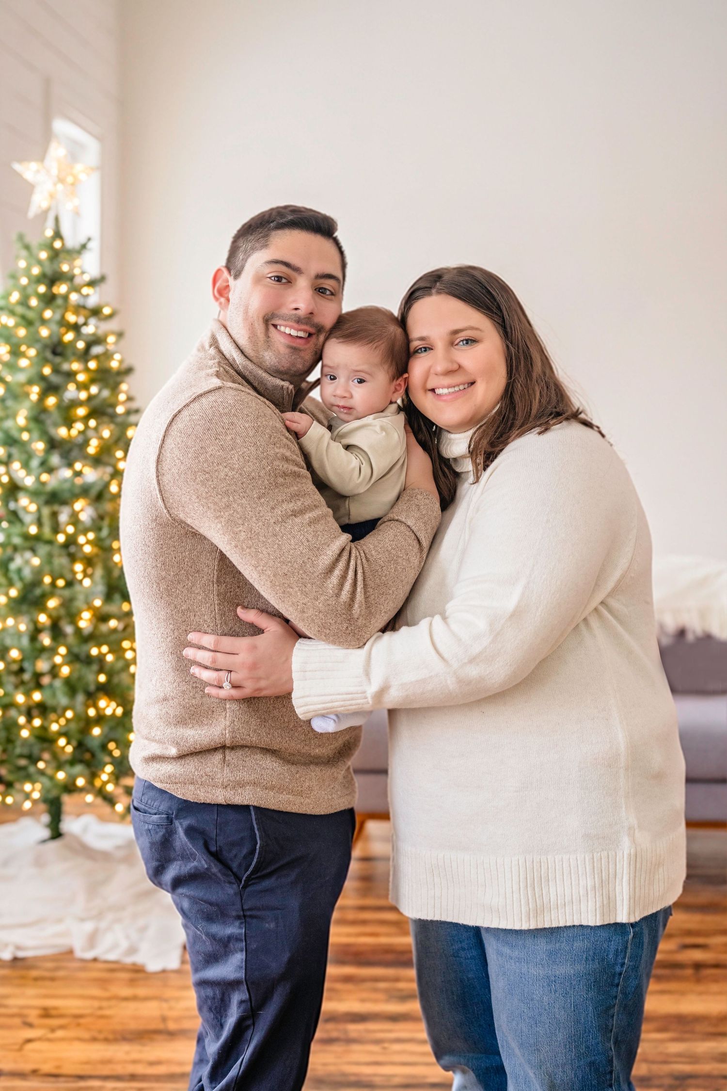Family shares tender holiday moments in front of  decorated Christmas tree in bright living room. Christmas family photoshoot.