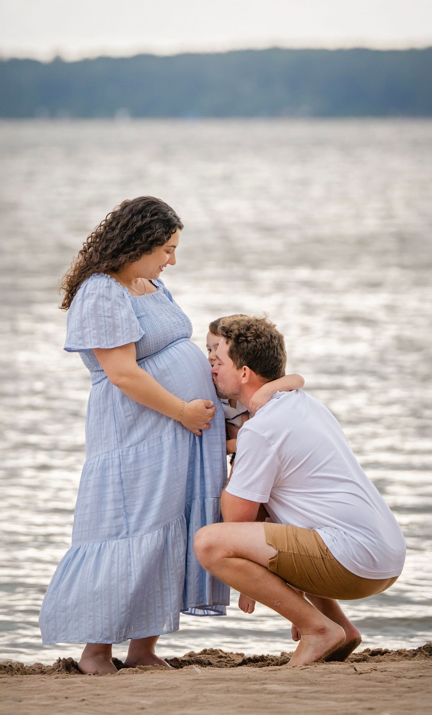 A couple shares an intimate moment on a beach with gentle waves and cloudy skies in the background.