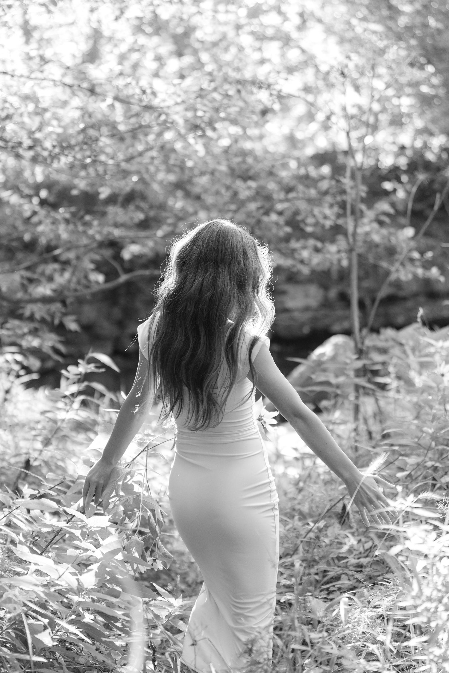 A person in a white tank top sits in a dreamy black and white garden setting surrounded by foliage.