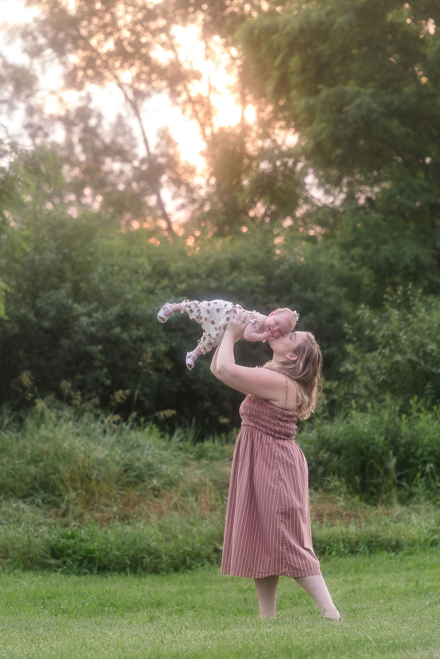Person in a striped dress twirling joyfully in a grassy field at sunset.