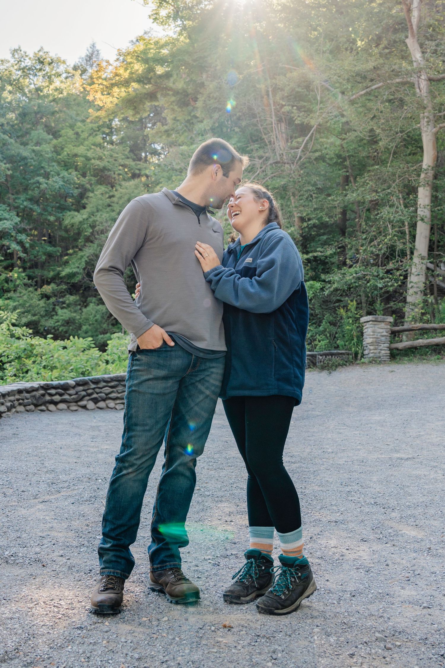 A couple shares a joyful moment together on a sunlit forest path during an autumn day.