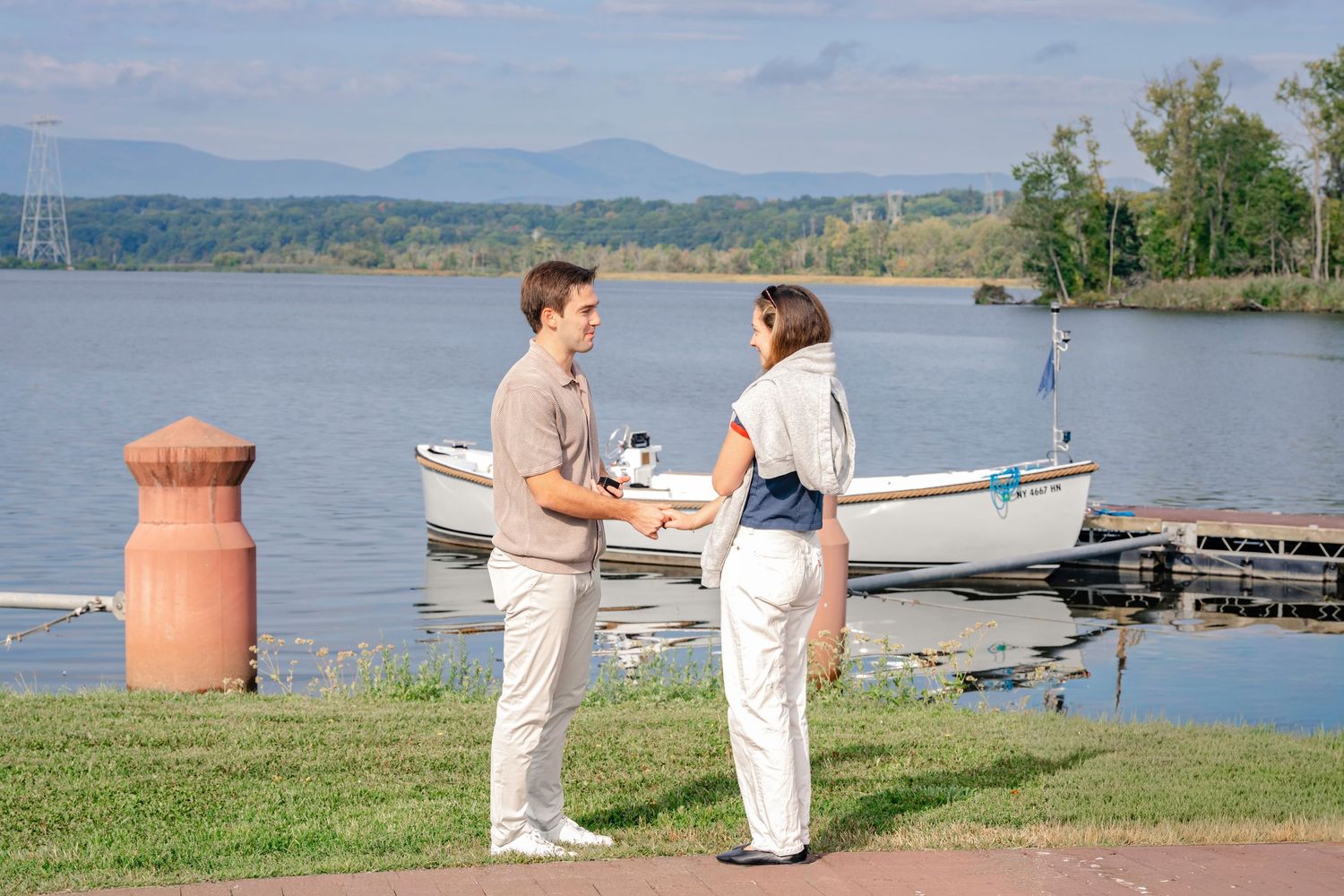 People enjoying a peaceful afternoon by a serene lake with mountains in the background and boats at the dock.
