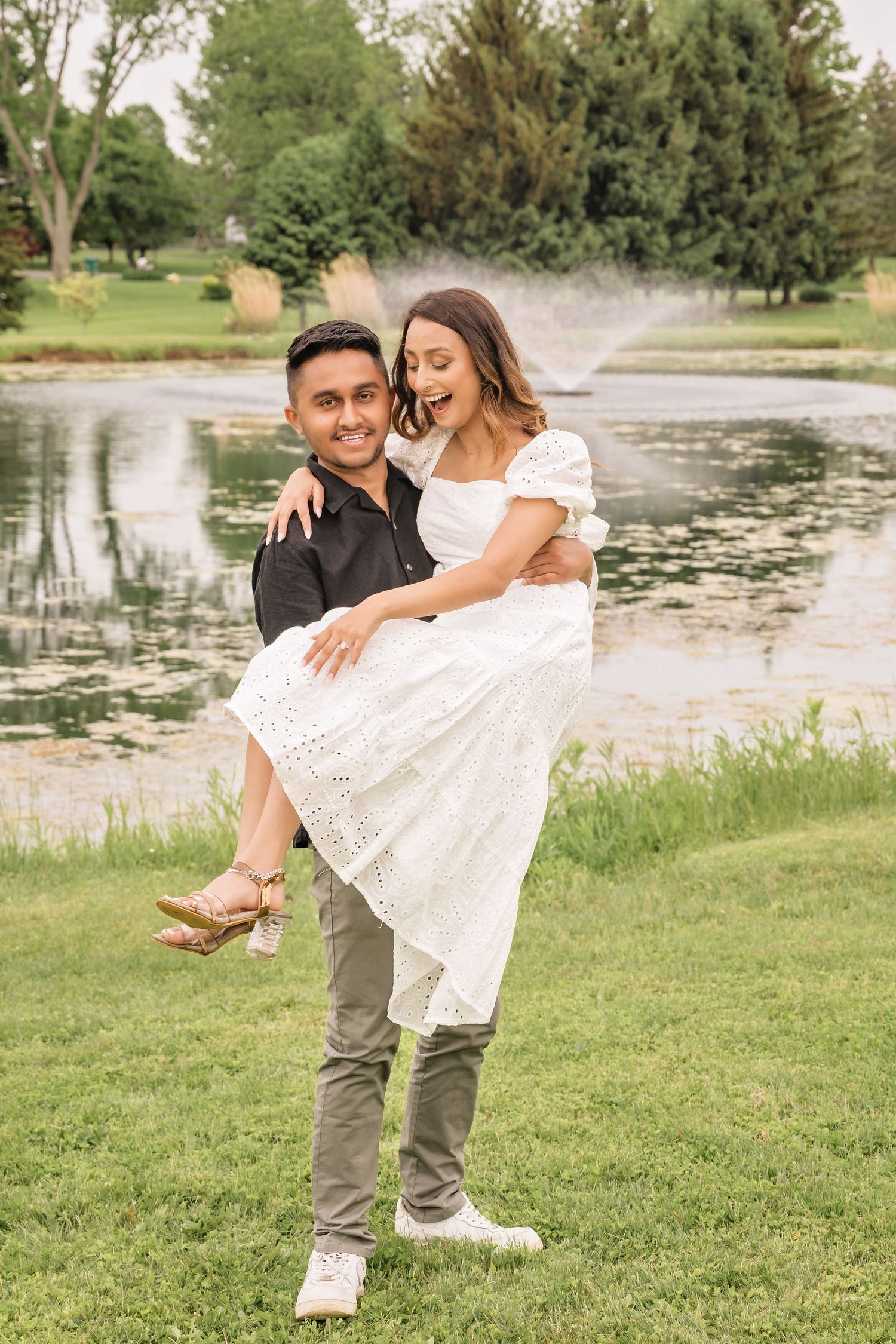 A playful couple dancing and twirling in a white dress and black shirt by a lake.