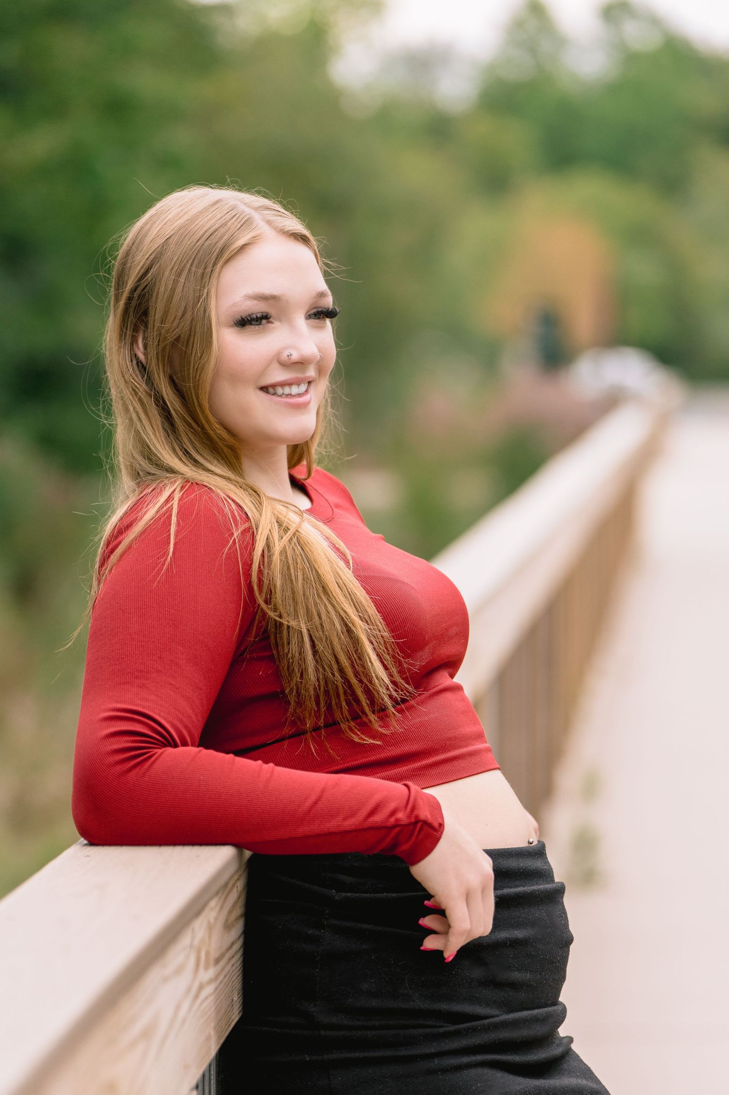 Person in red and black outfit poses playfully in outdoor setting with natural greenery in background.