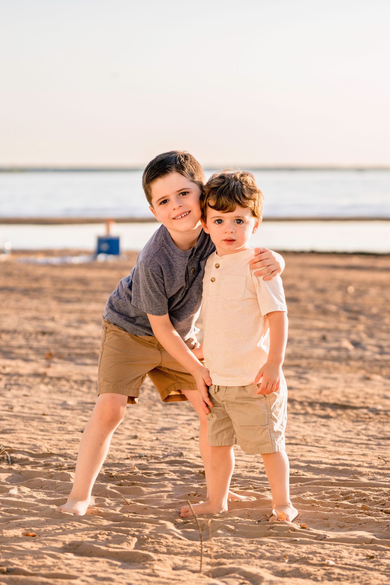 Two children playfully interact on a sandy beach during sunset, casting long shadows on the sand.