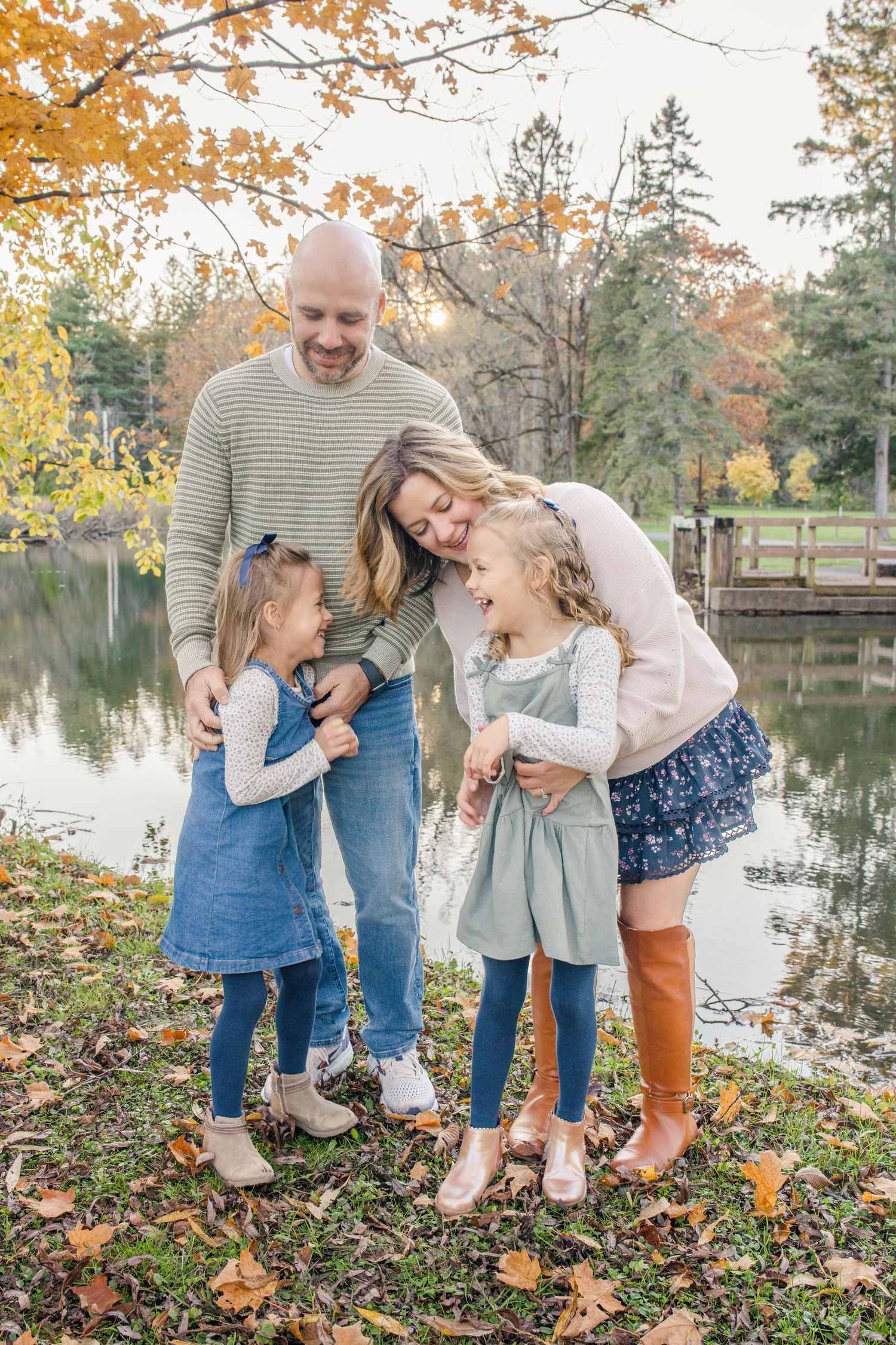 A family shares joyful moments together on an autumn day by a lake with golden leaves scattered on the ground.