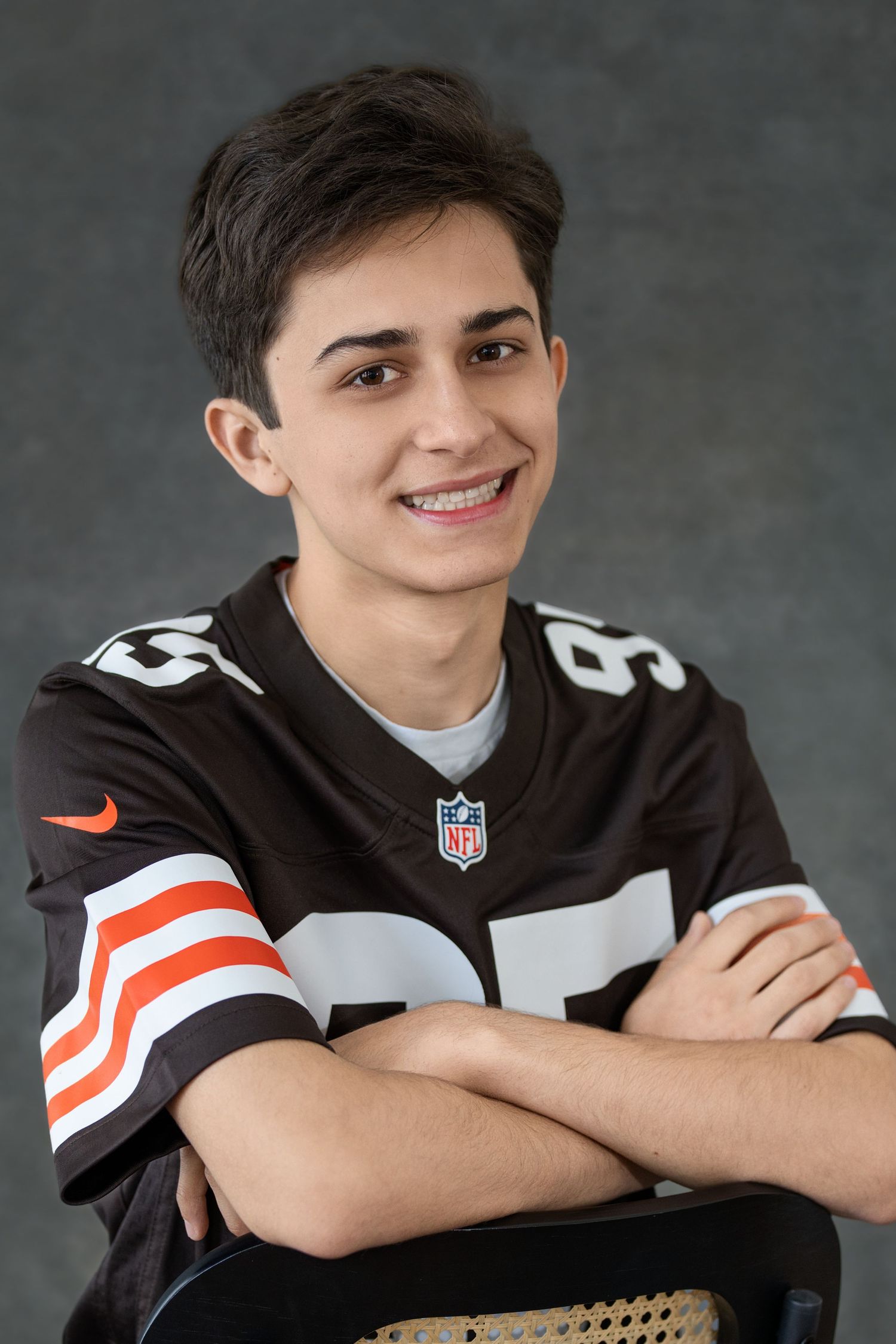 Senior portrait wearing Cleveland Browns NFL jersey in casual seated pose against gray backdrop.