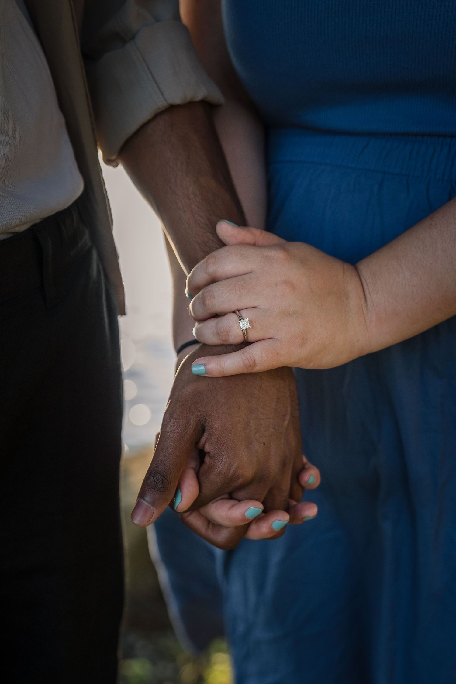 Close-up shot of hands holding each other with teal painted fingernails against a dark blue background.