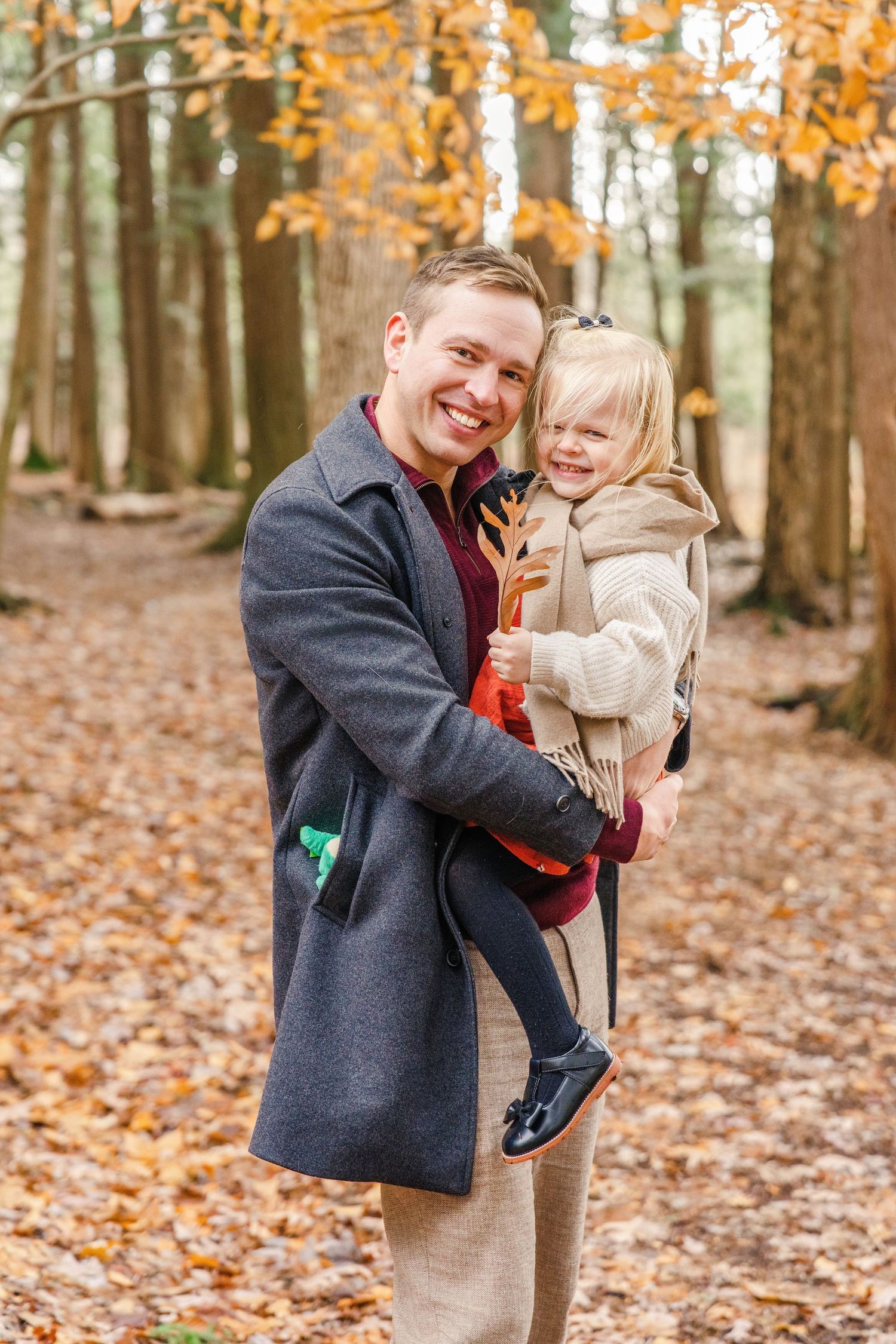Two people share joyful moments together in a forest filled with fallen autumn leaves and golden foliage.