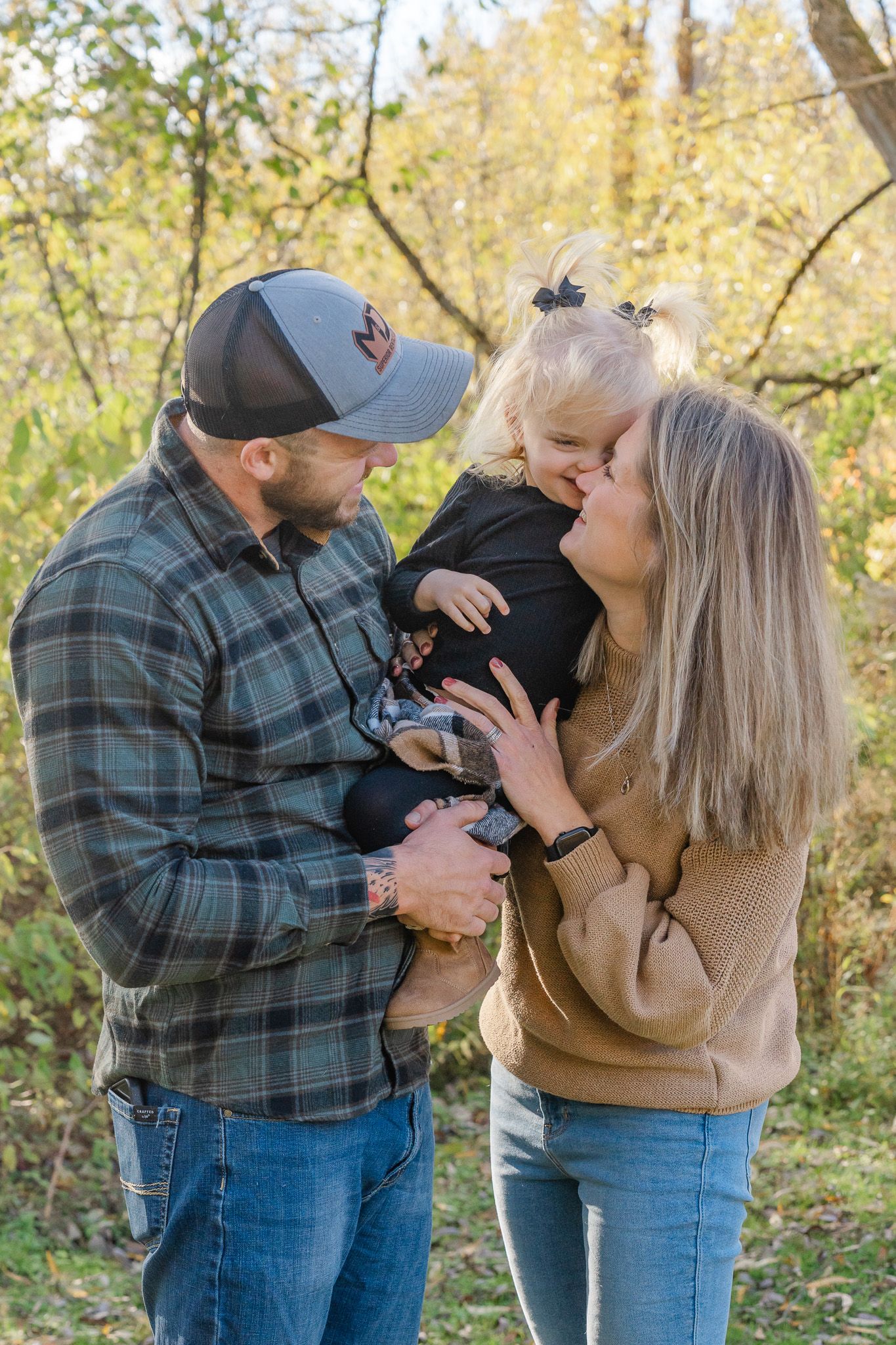 A couple shares tender moments with their baby in a series of autumn outdoor photos with golden foliage.