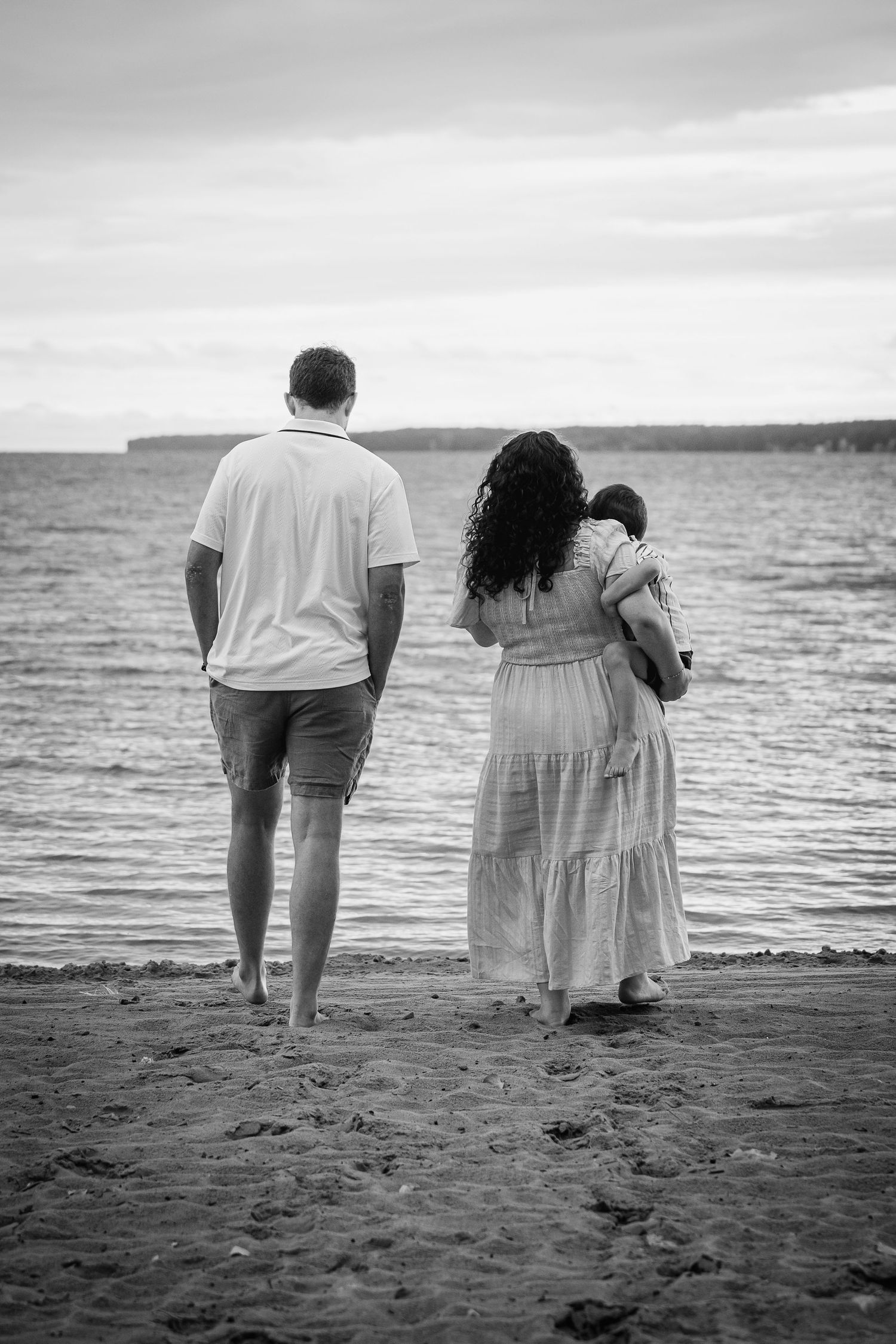 Black and white photo of people standing together on a beach looking out at the calm ocean waters.