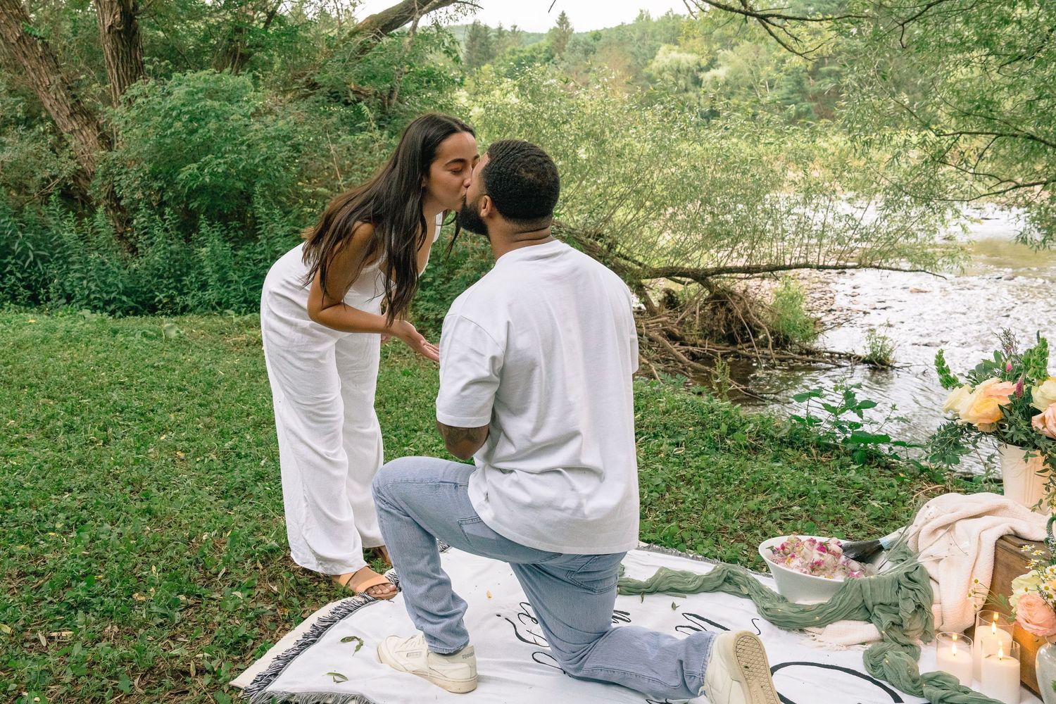 Couple enjoying a romantic picnic by the river on a sunny summer afternoon.