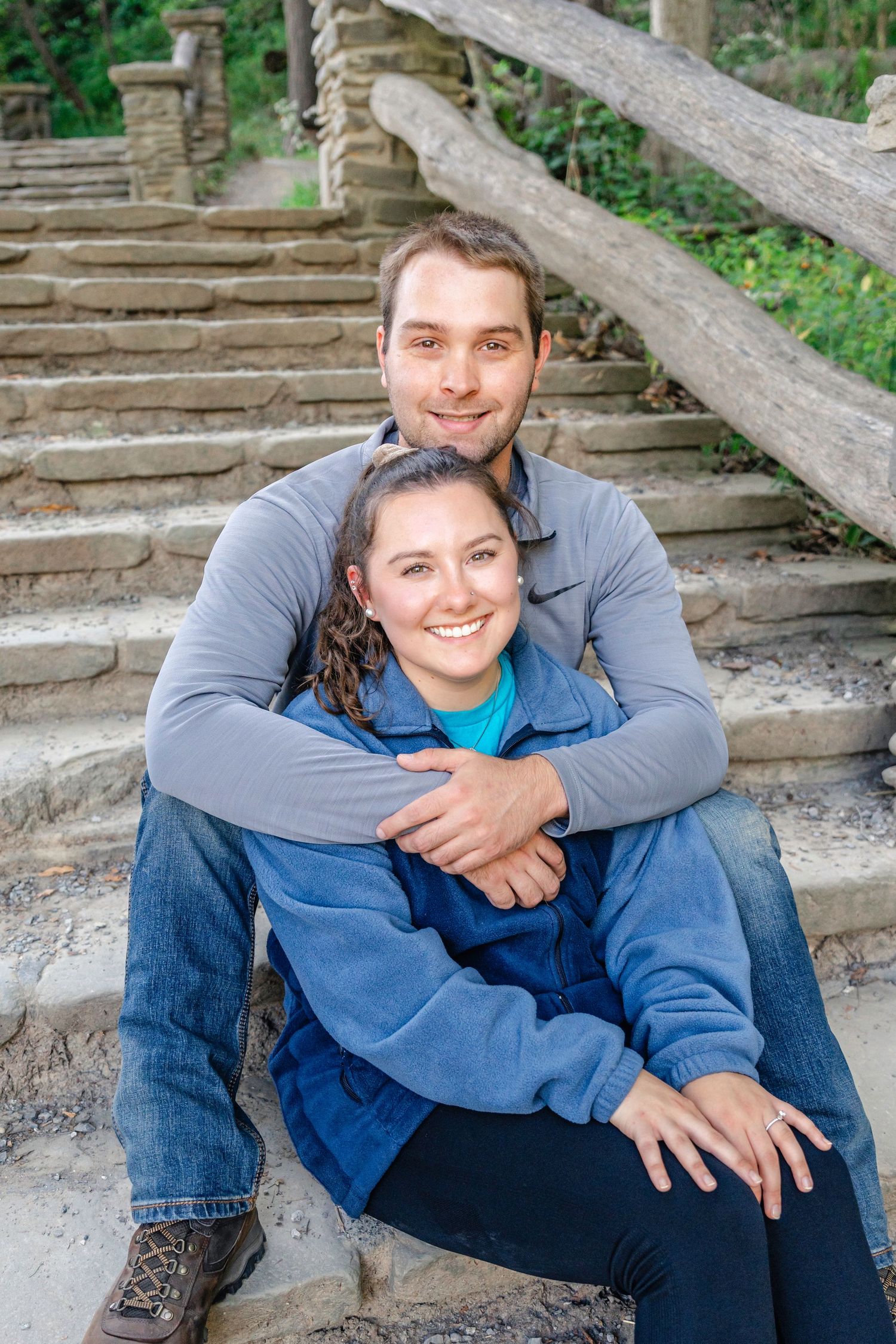 A couple sits together on rustic stone steps surrounded by greenery in casual denim and blue clothing.