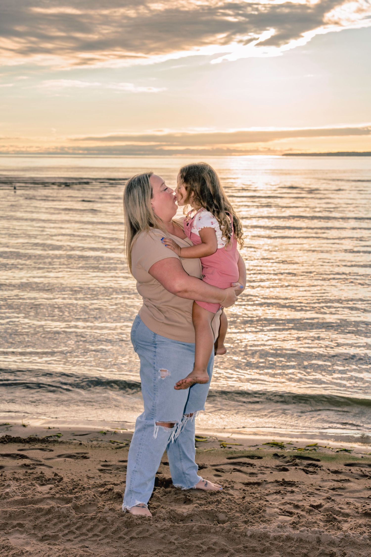 A loving moment captured between two people embracing on a beach at sunset with golden light reflecting off the ocean.