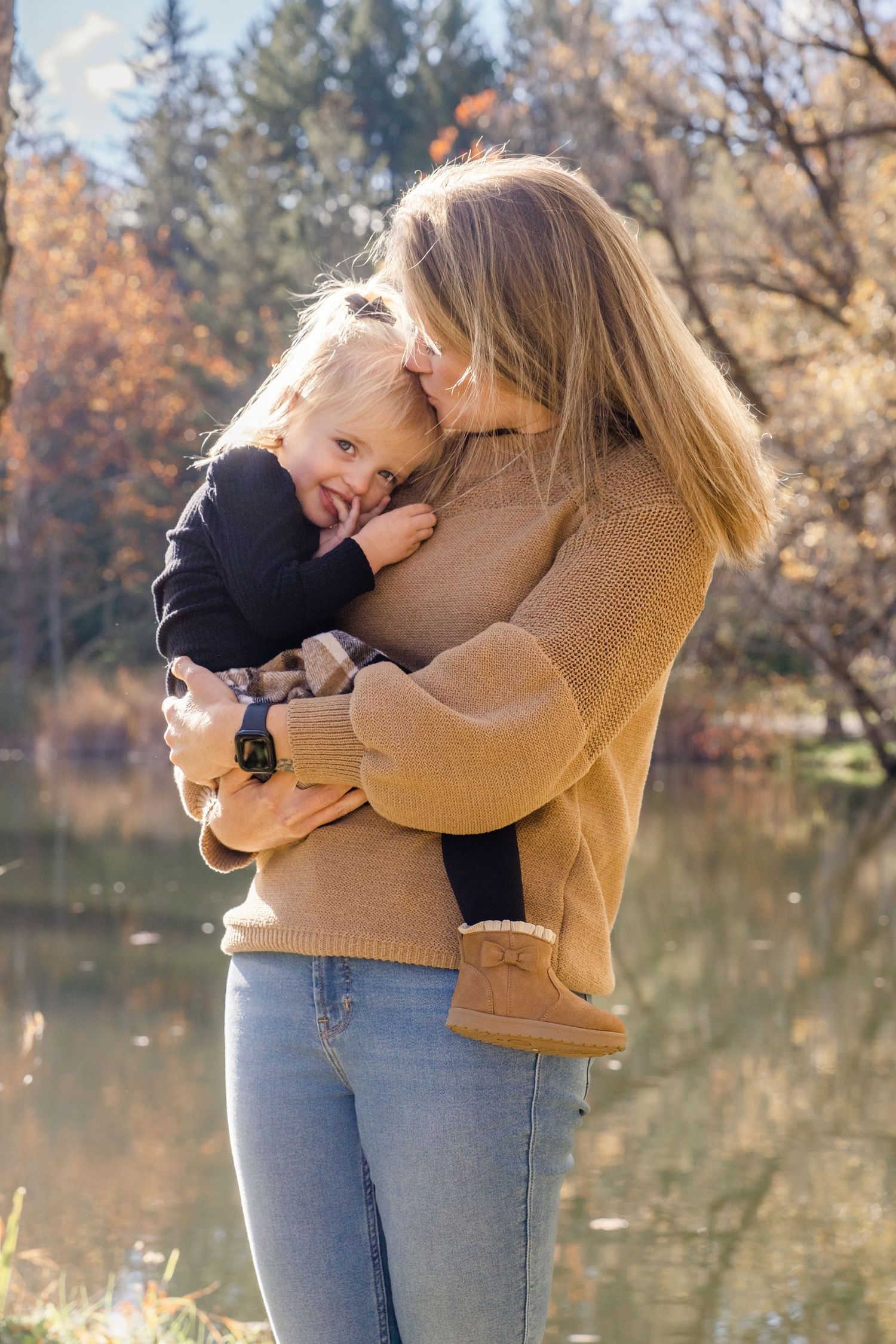 A series of tender moments captured by a lake showing affectionate embraces in autumn with light brown sweater and jeans.