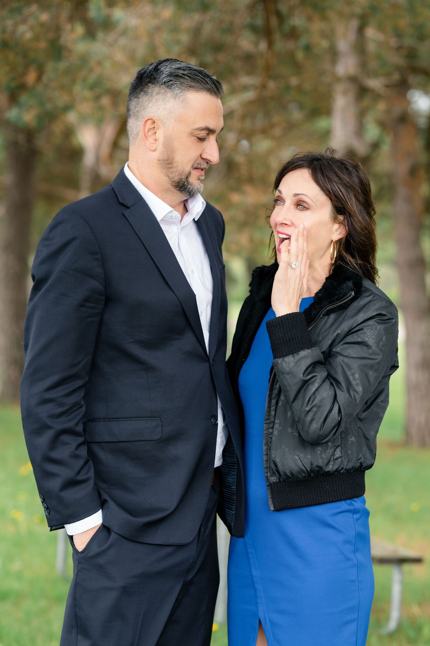 A couple shares a sweet moment outdoors, with one person in a blue dress and another in a black suit.