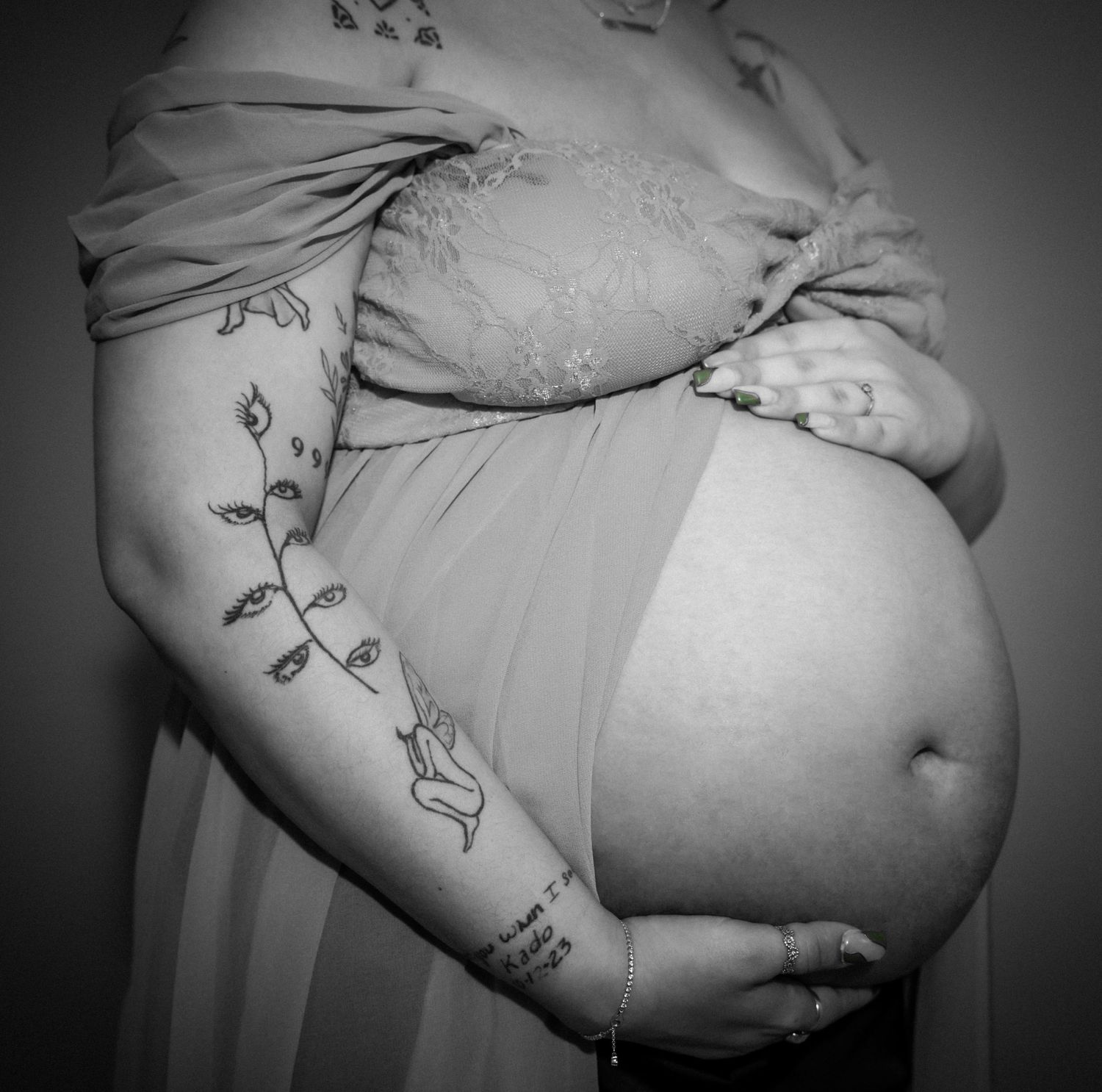 Black and white view of a pregnant belly with delicate floral vine tattoos decorating the arm.