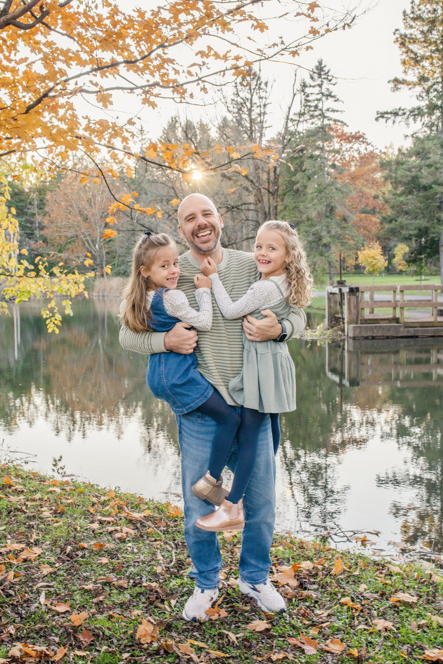 Family enjoying a playful autumn moment by a serene lake with golden fall foliage reflecting in the water.