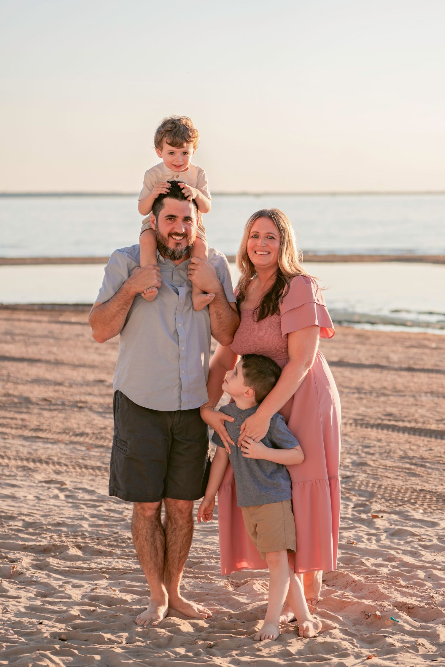 A family enjoys a playful moment together on a sandy beach at sunset.