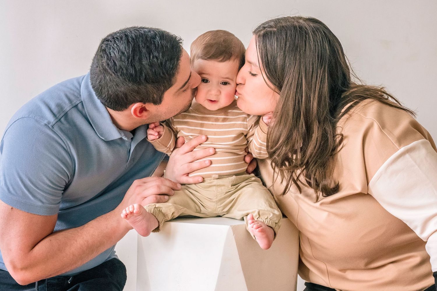 Parents kissing their adorable baby on the cheeks during a professional family portrait session.