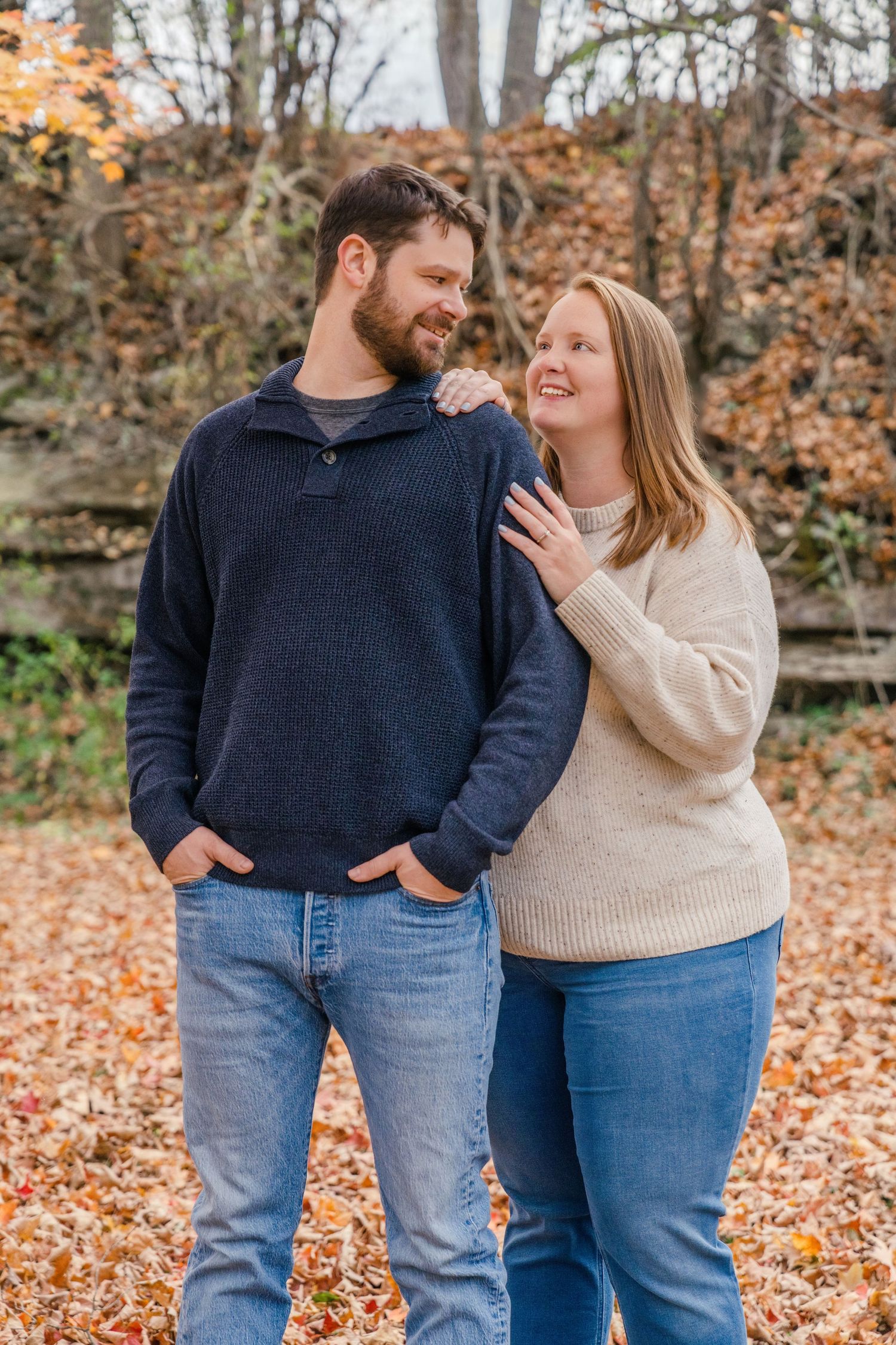 A couple shares joyful moments together while standing in autumn leaves on a fall day. Engagement session.