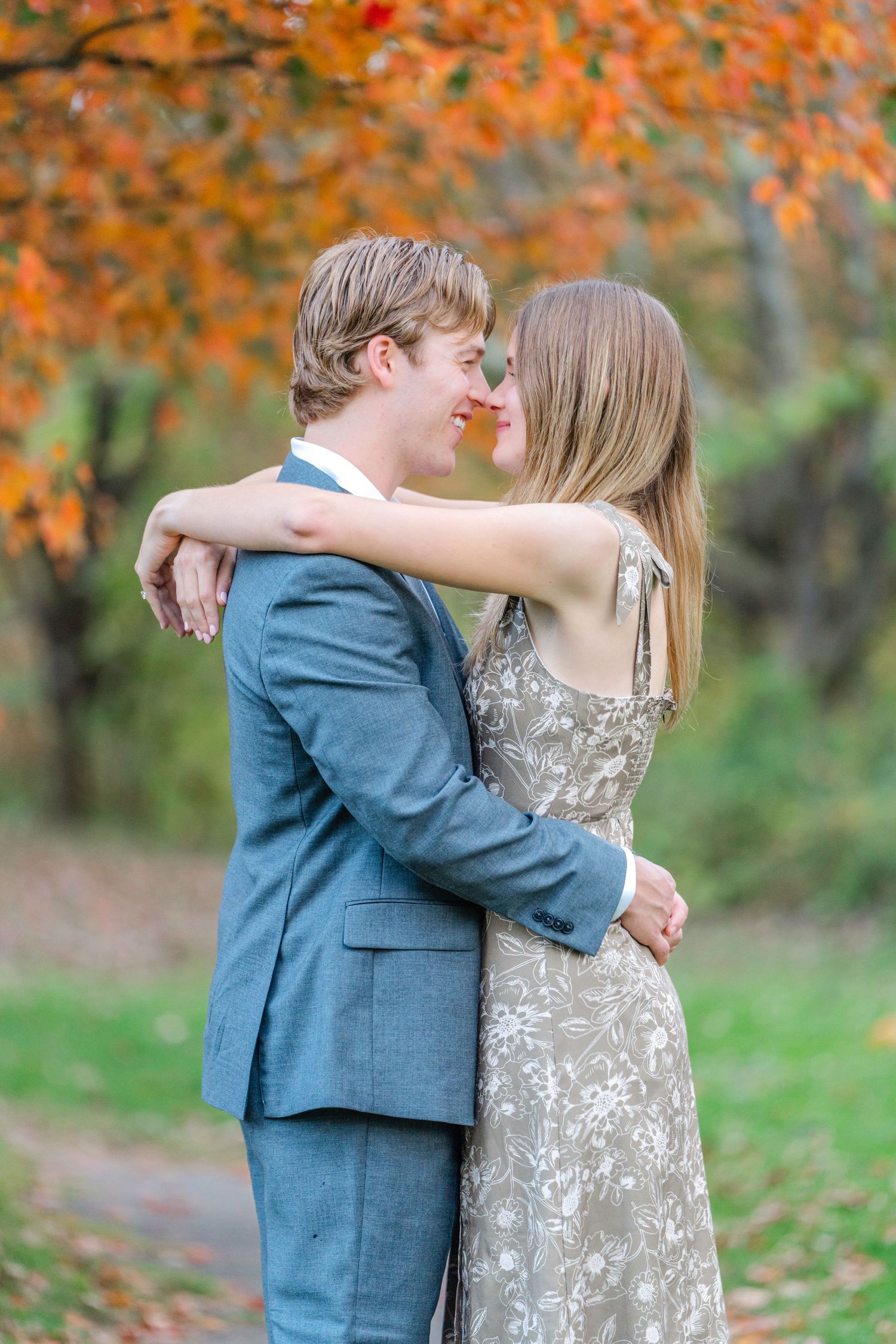A couple embraces outdoors in autumn, with orange fall foliage in the background.
