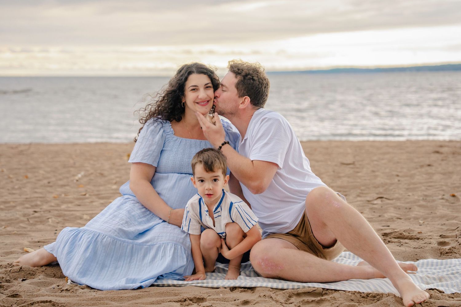 A family shares tender moments together on a sandy beach during golden hour.