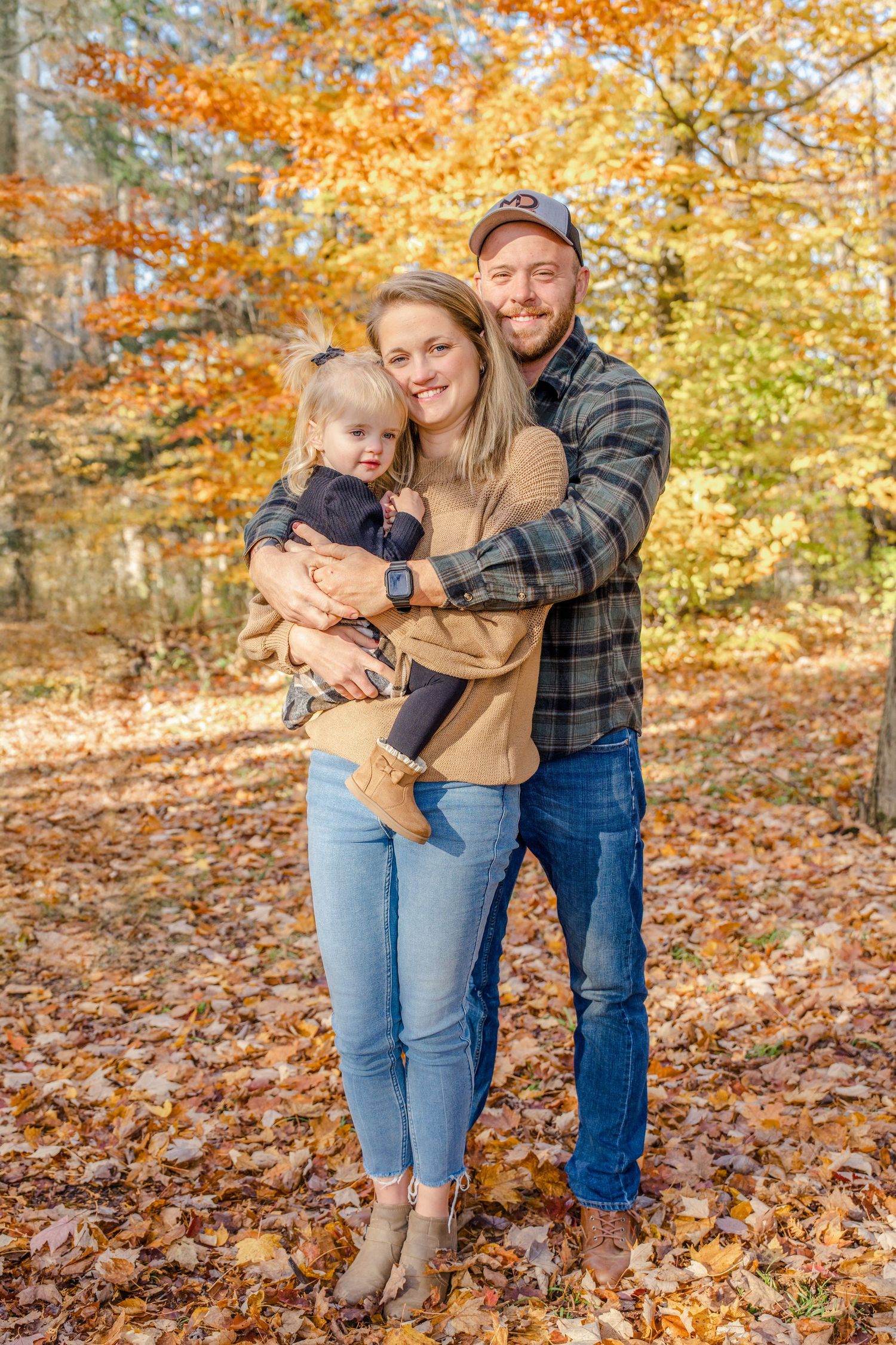 A family poses together in a wooded area with vibrant fall foliage and scattered autumn leaves on the ground.