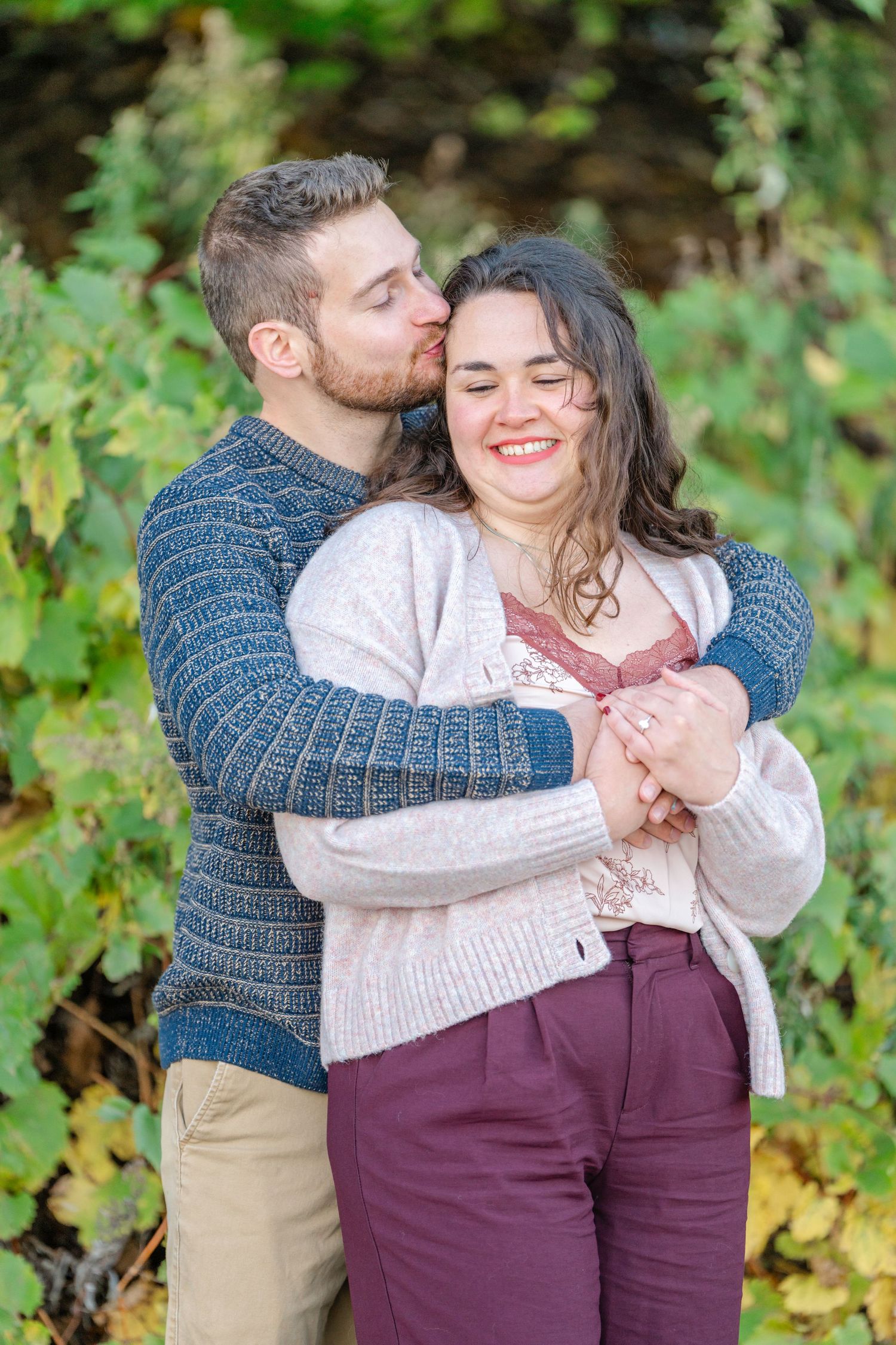 A romantic autumn photoshoot showing a couple embracing outdoors with fall foliage in the background.