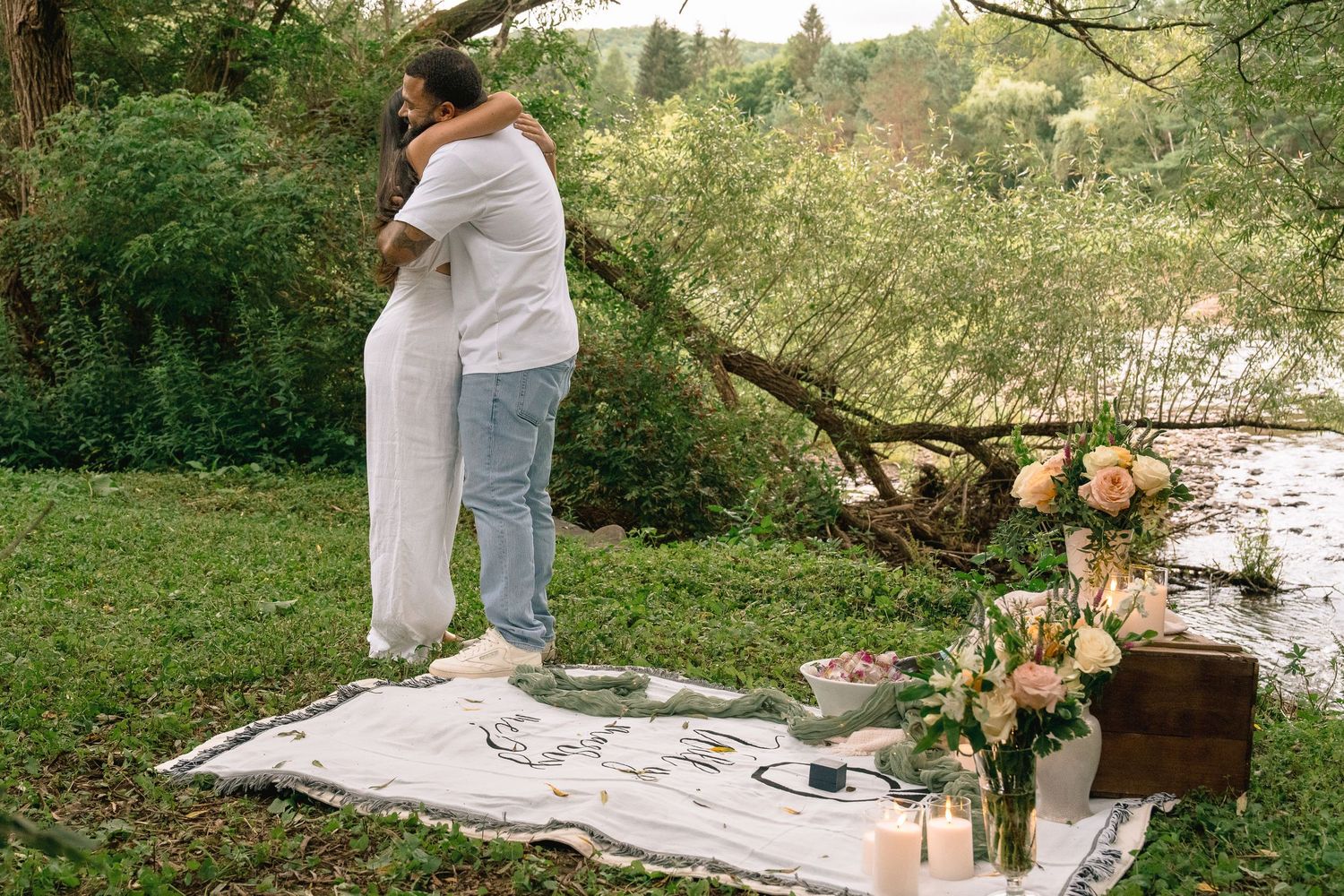 A romantic picnic setup in a lush forest setting with a blanket, flowers, and decorative elements.