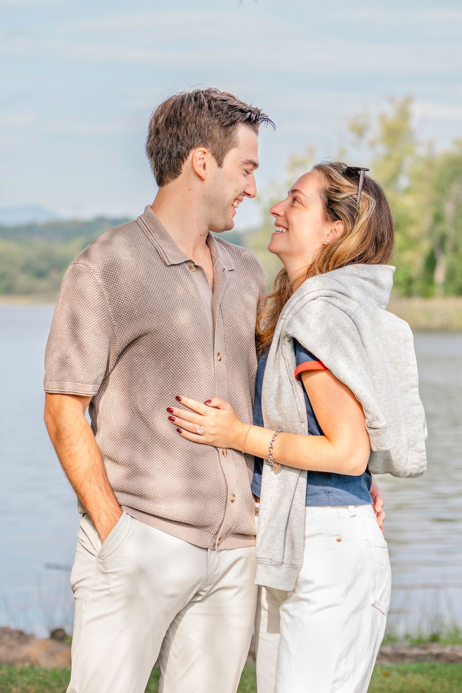 A couple shares romantic moments by a lakeside wearing coordinated beige and white outfits in a natural outdoor setting.