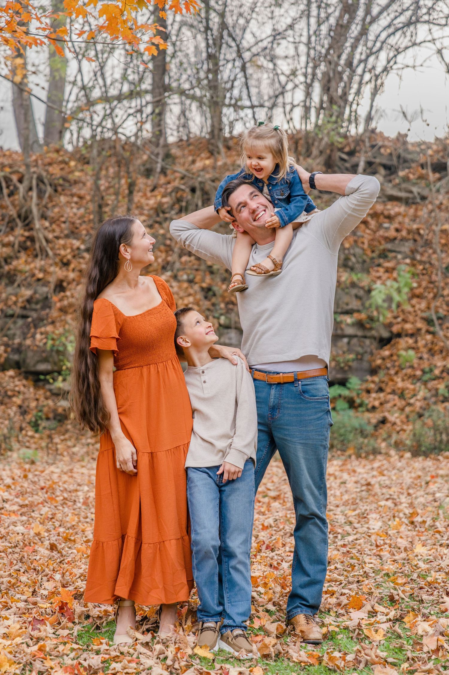 A family enjoys a playful autumn moment together in a forest filled with fallen orange leaves.