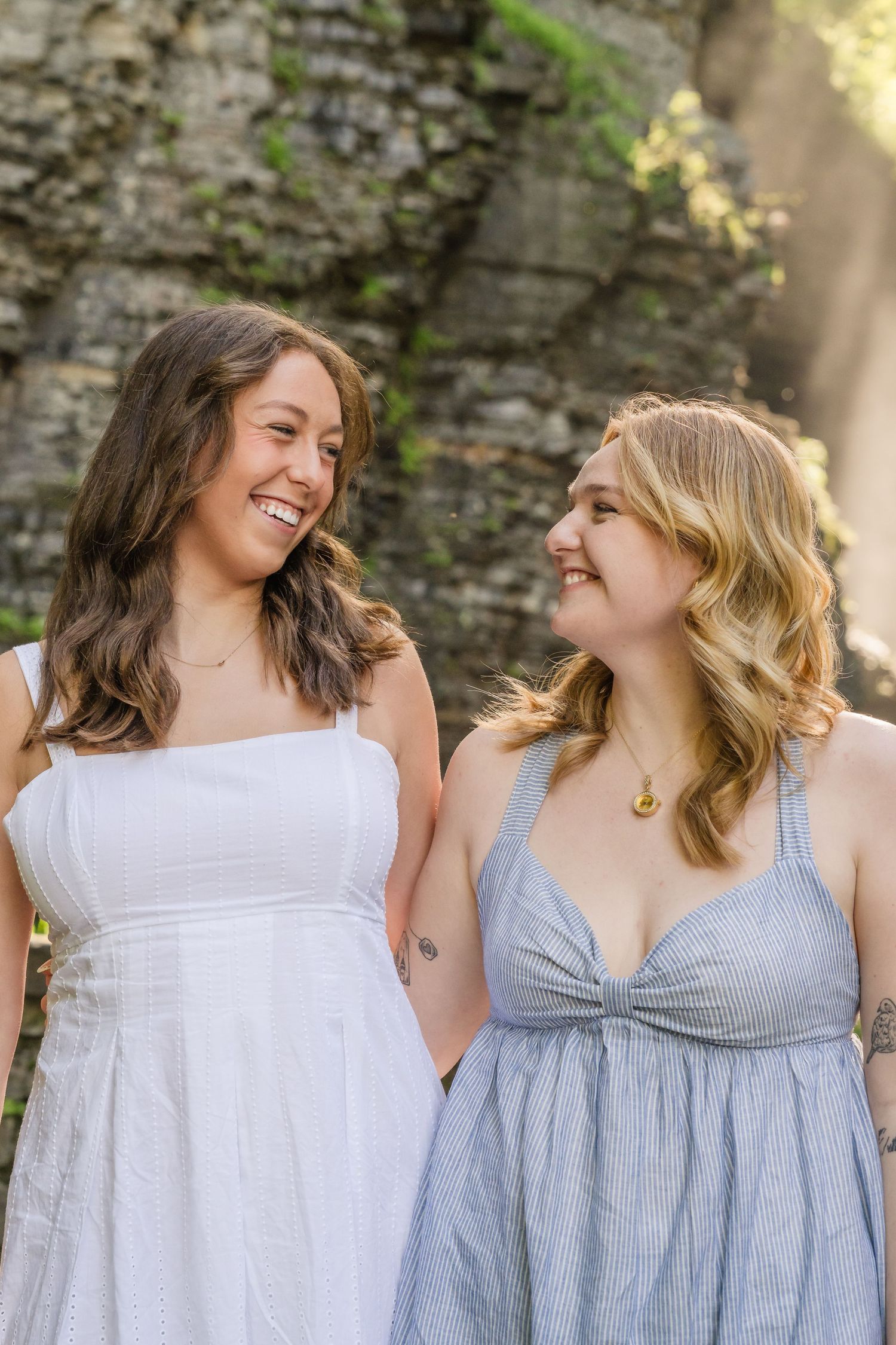 Two people wearing light blue and white sundresses smile and laugh together in a series of candid outdoor photos.