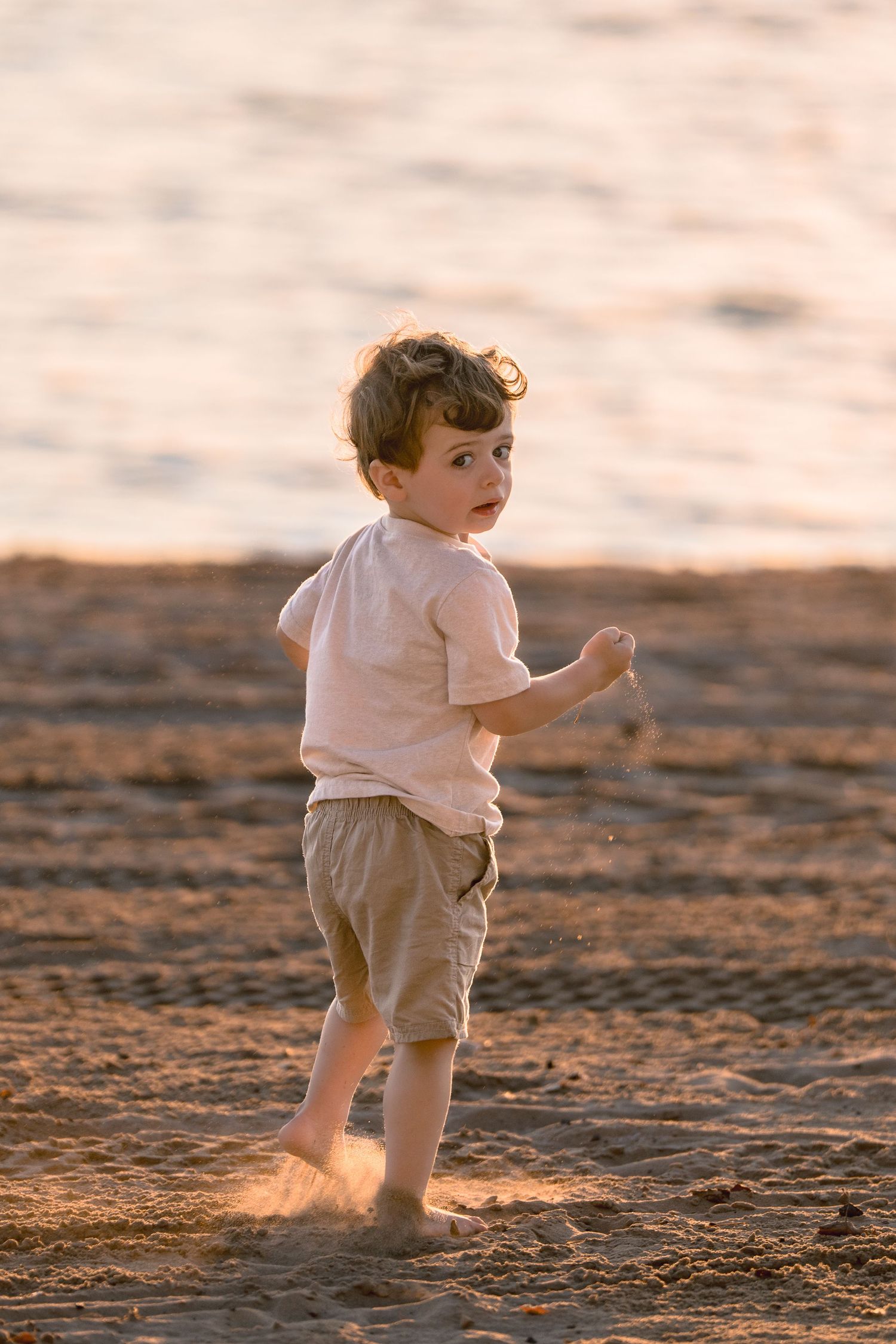 Small child runs playfully along sandy beach at sunset creating footprints in golden light.