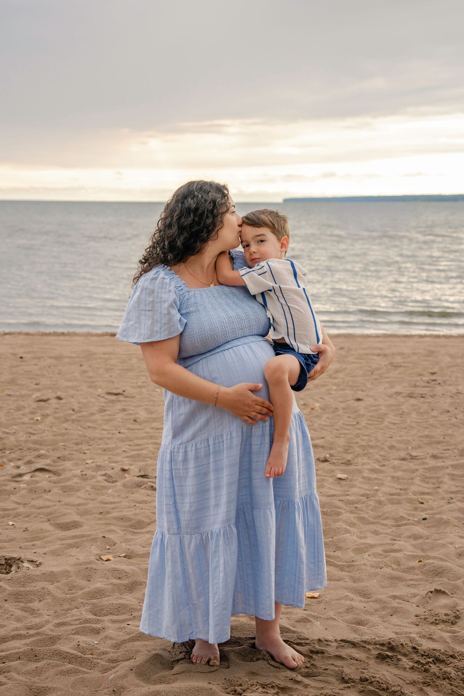 A family embraces while wearing coordinating blue outfits during a sunset photoshoot on a sandy beach.