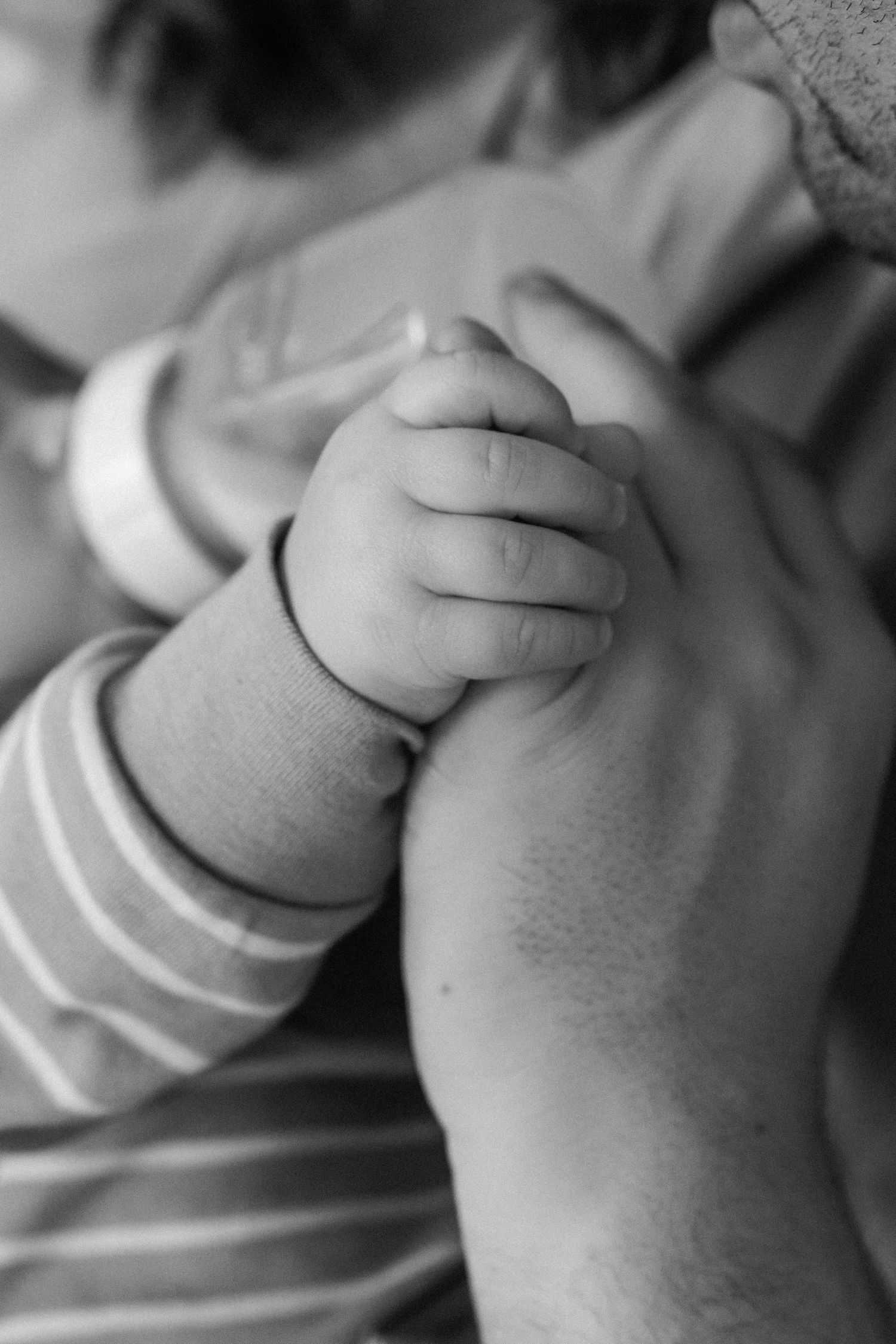 Black and white close-up of baby hand holding adult finger.