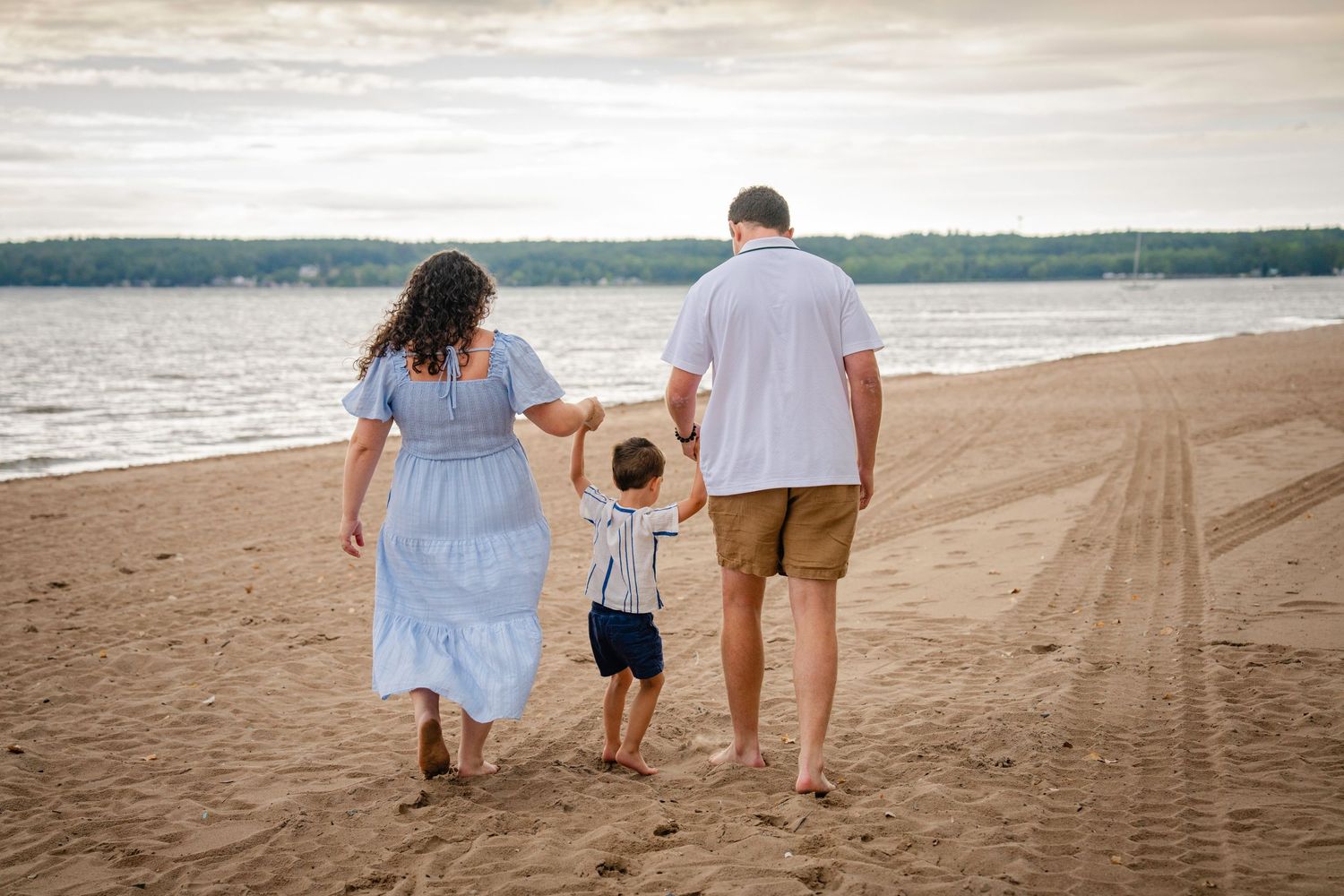 Family walking together hand in hand along a sandy beach at sunset with ocean waves in the background.
