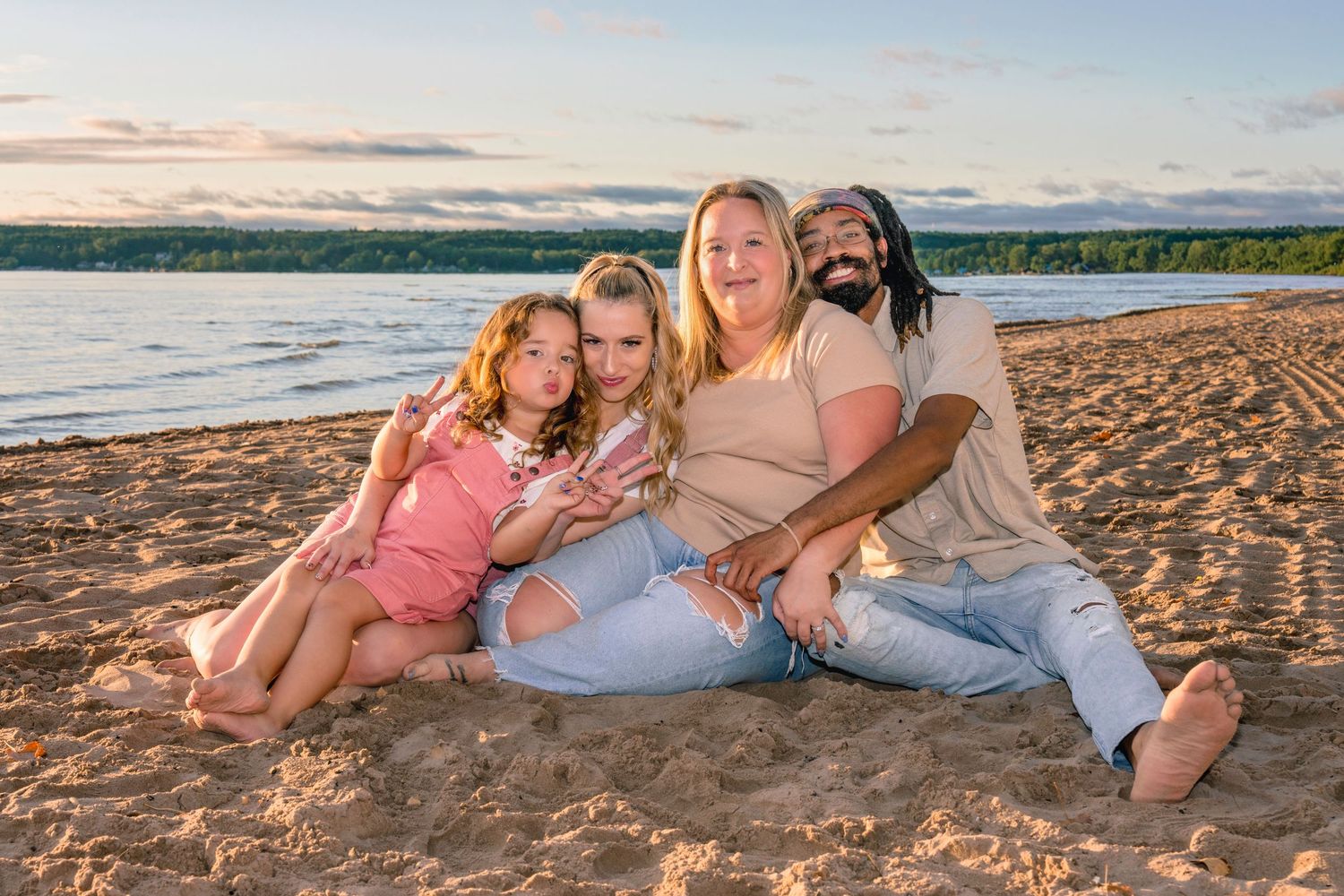 Family relaxing on beach sand during golden hour with ocean waves in background.