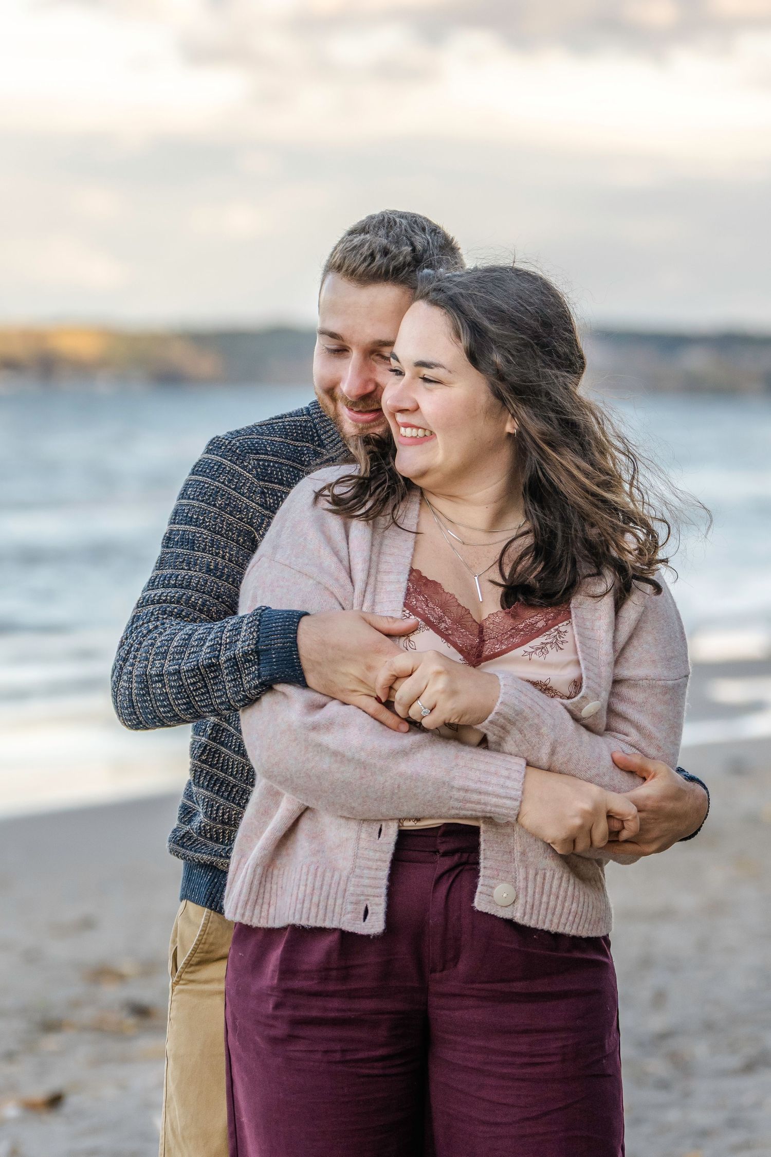 A romantic couple shares tender moments and laughter while embracing on a beach at sunset.